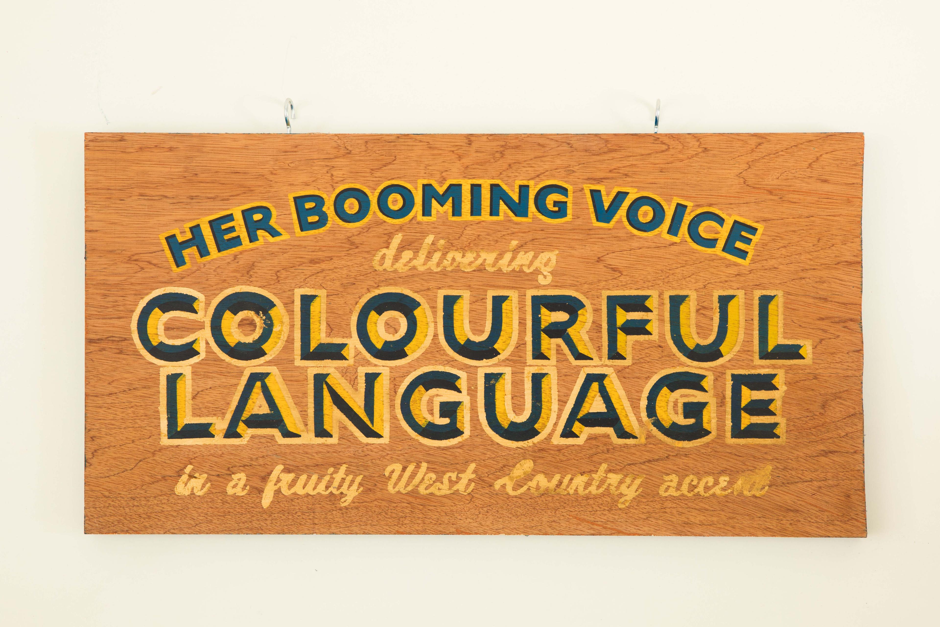 A fairground sign with the bold text: her booming voice delivering colourful language in a fruity west country accent.