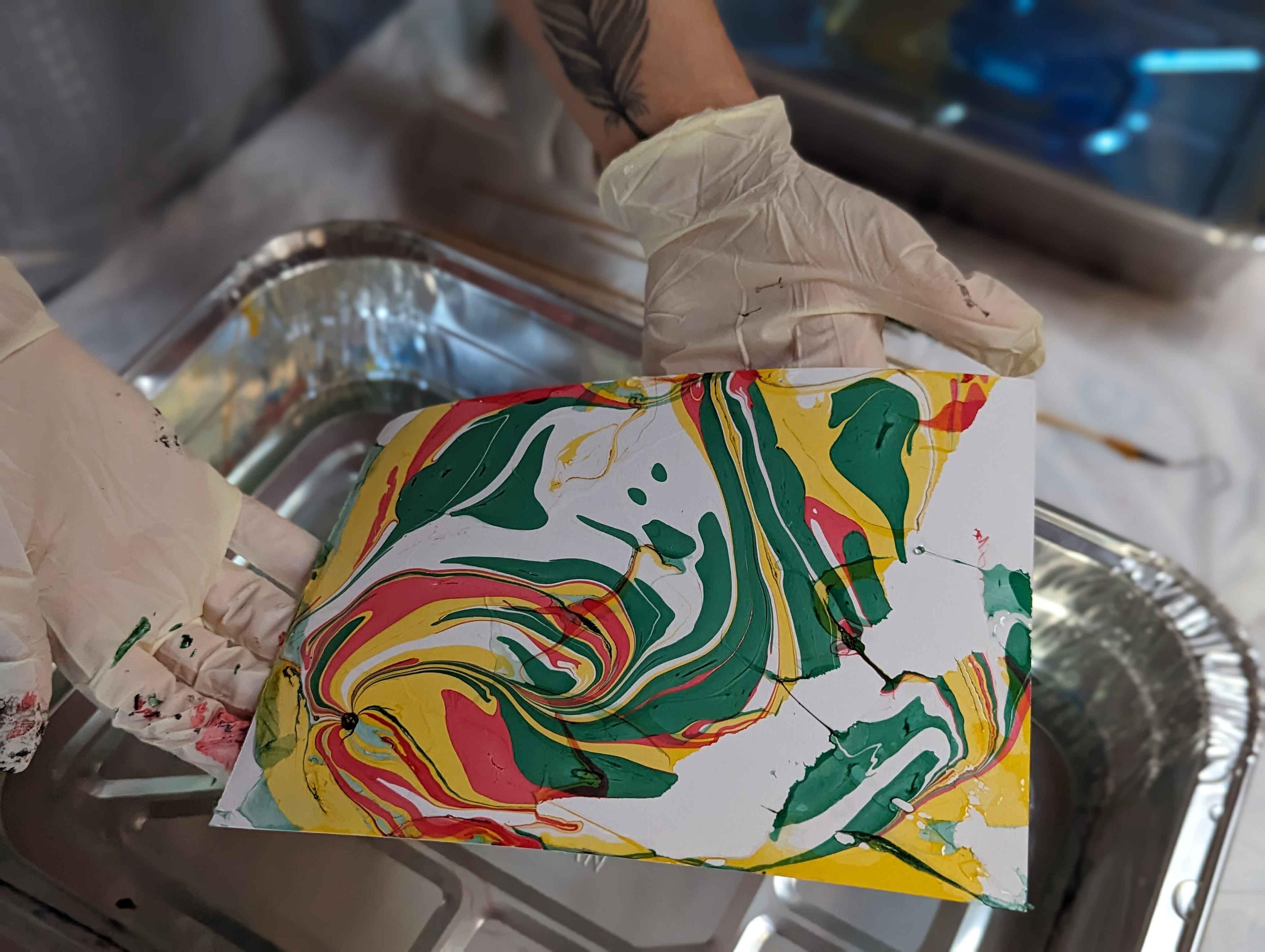 A pair of gloved hands holding up a piece of marbled paper.