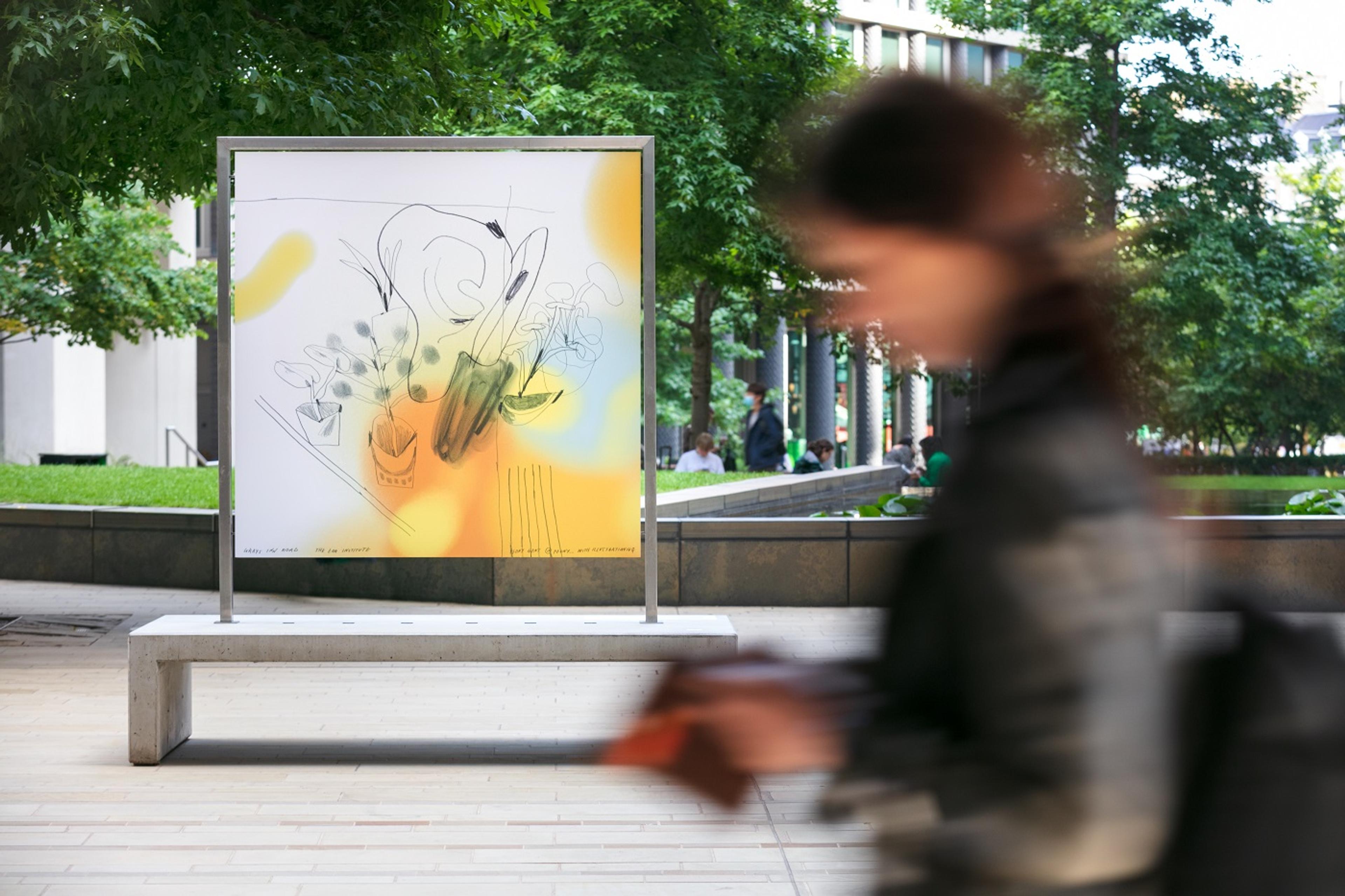 Freestanding large print installed outside with trees in the background and a person blurred out in the foreground