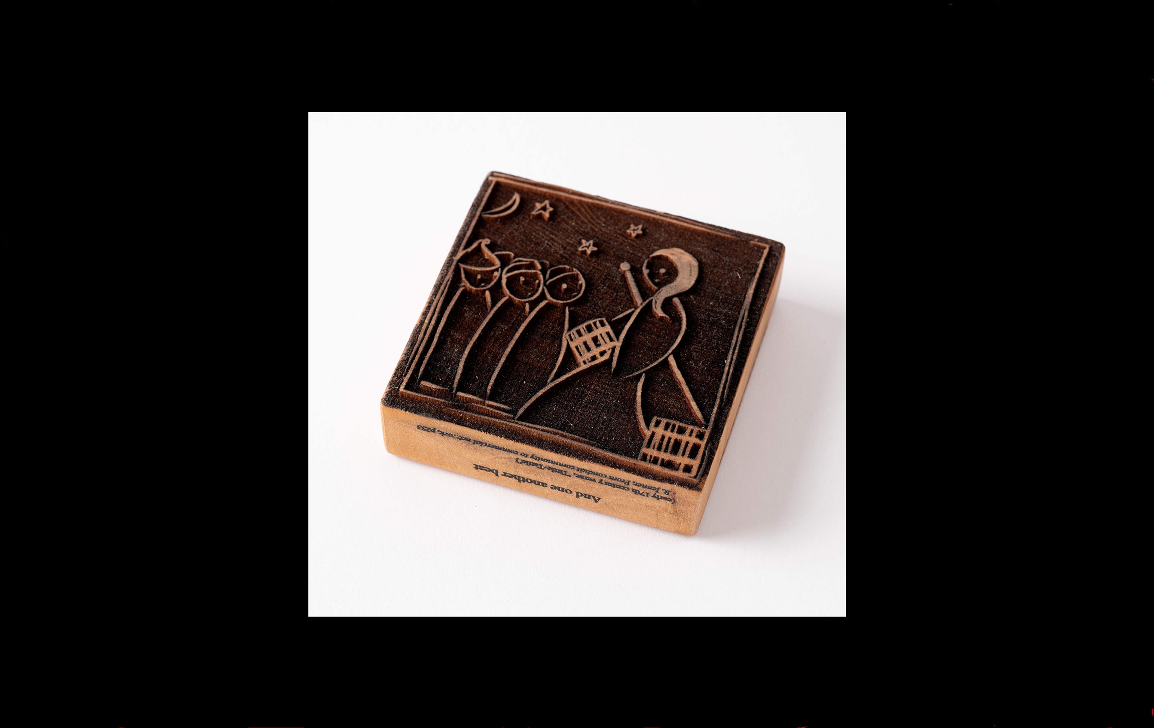 Wooden block with an image of a woman carrying water buckers with three smaller people under the moonlight etched into the surface