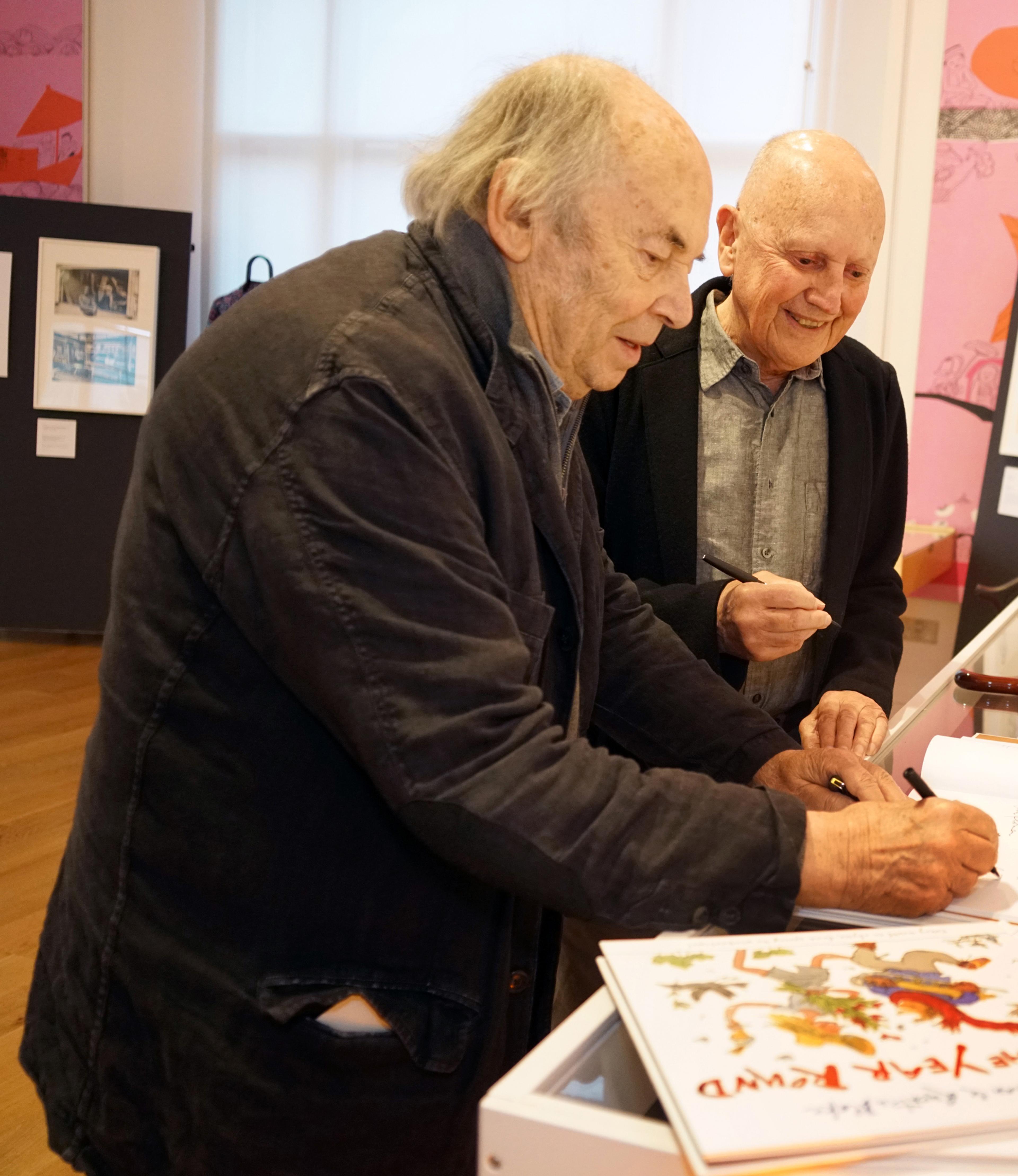 Two people in an exhibition space, signing books.