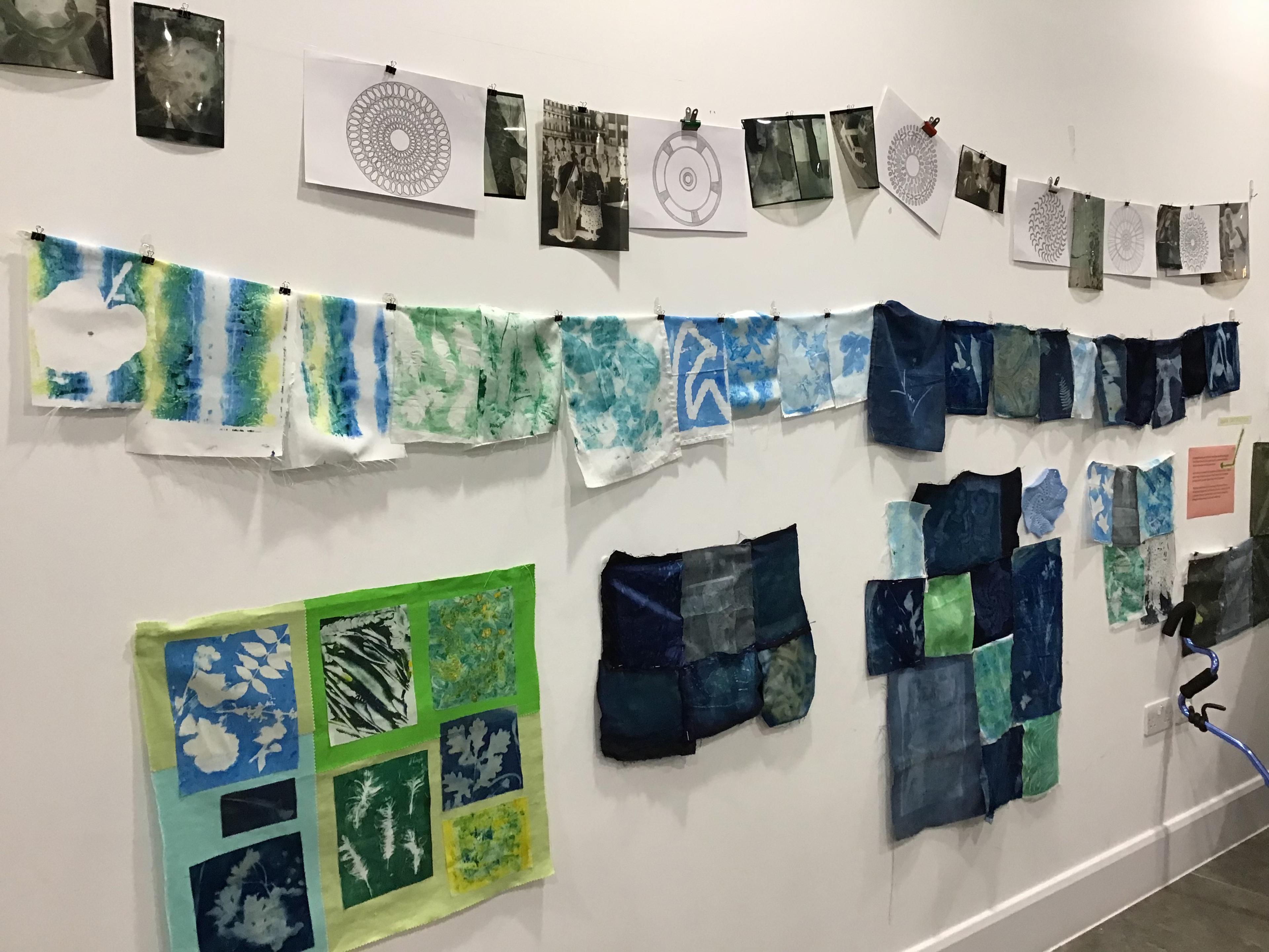 Fabric and paper illustrations displayed  hanging on a wall.