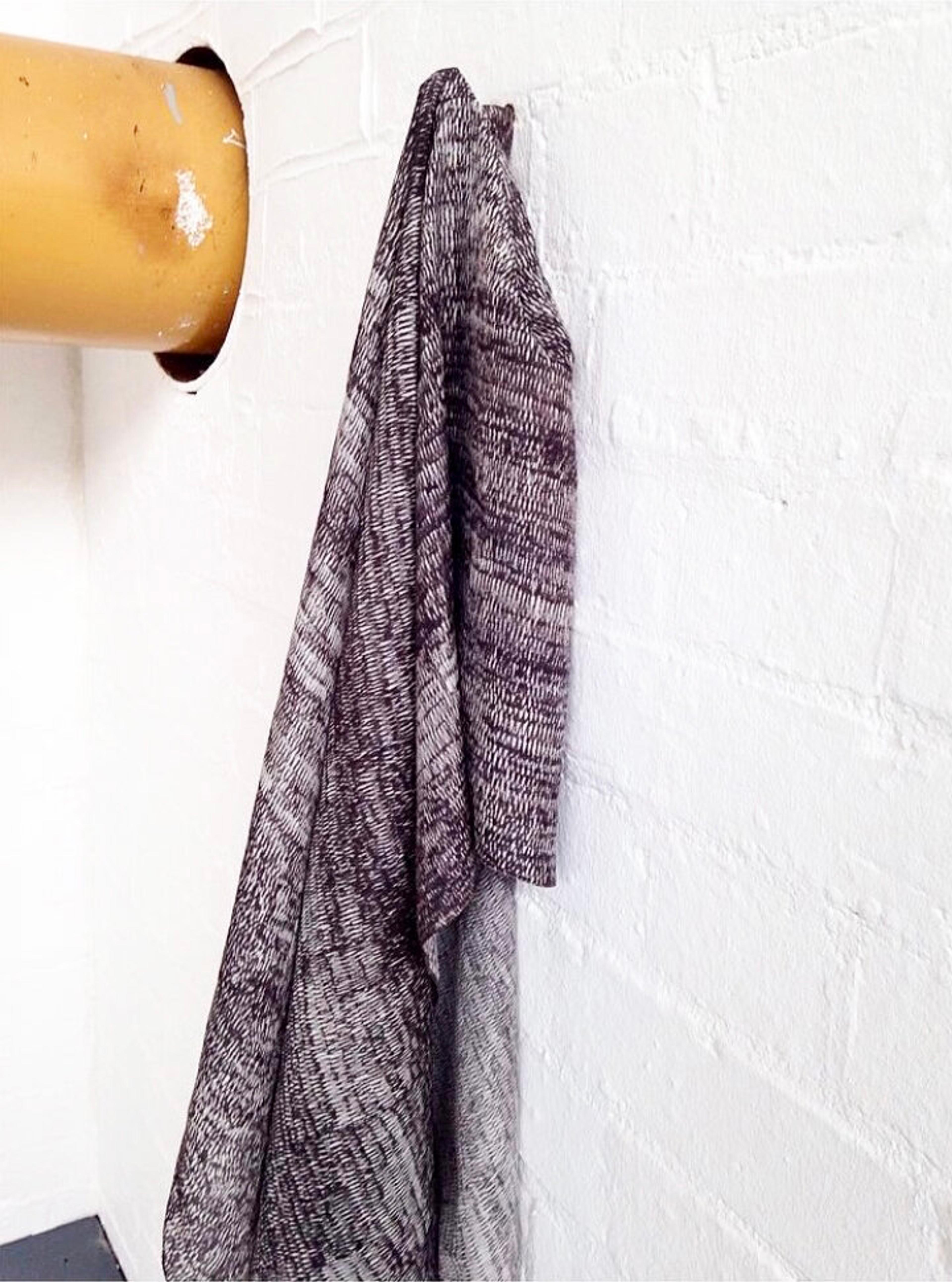 A patterned textile hanging from a hook on a white wall.