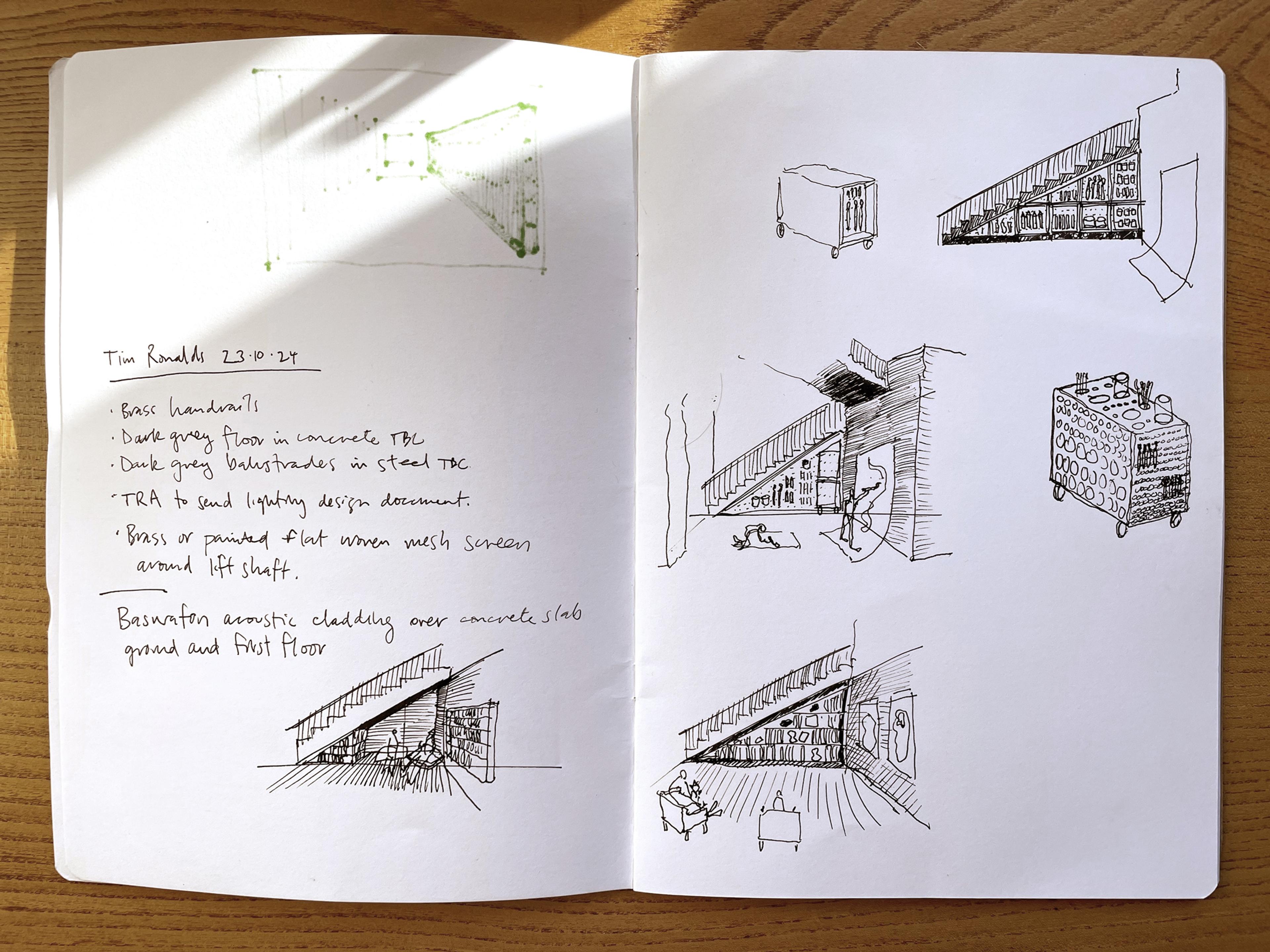 A photograph of an open sketchbook on a wooden desk. On the pages are sketches and notes in black pen of a staircase, bookcases and furniture in the corner of a room