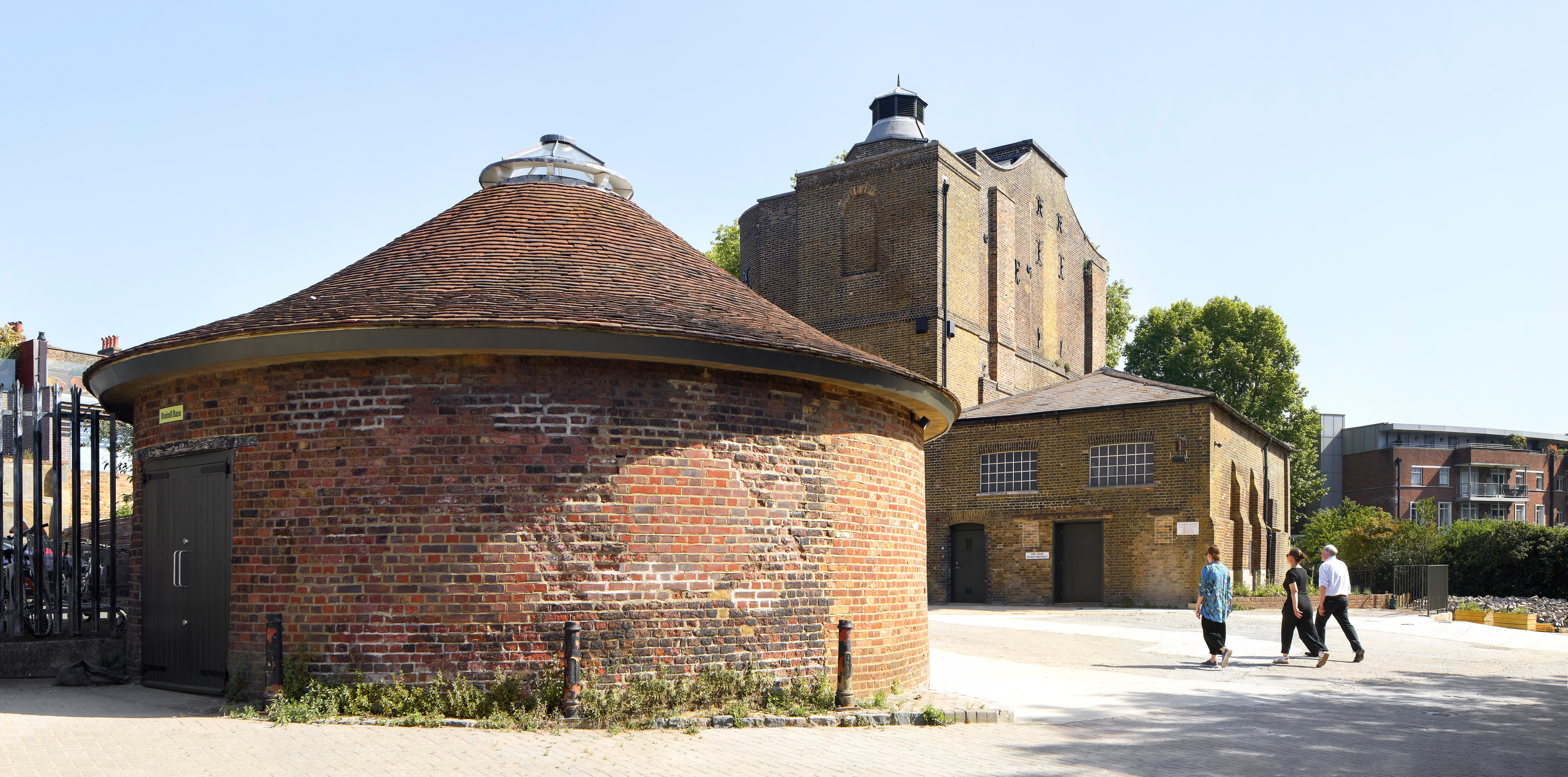 Exterior of old brick buildings with three people walking in the sunlight.