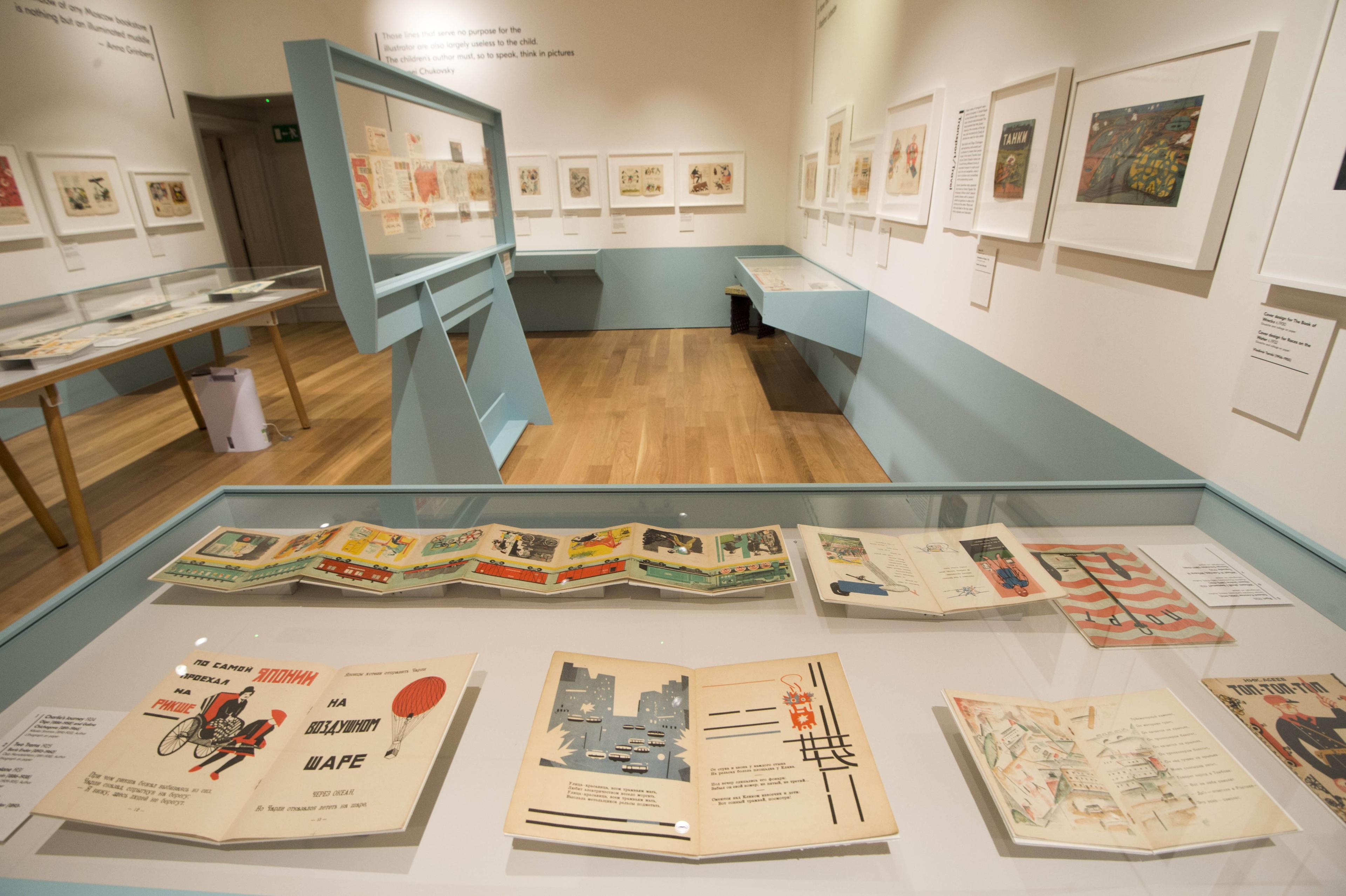  Inside an exhibition space with framed illustrations on the wall and displayed in glass cabinets.