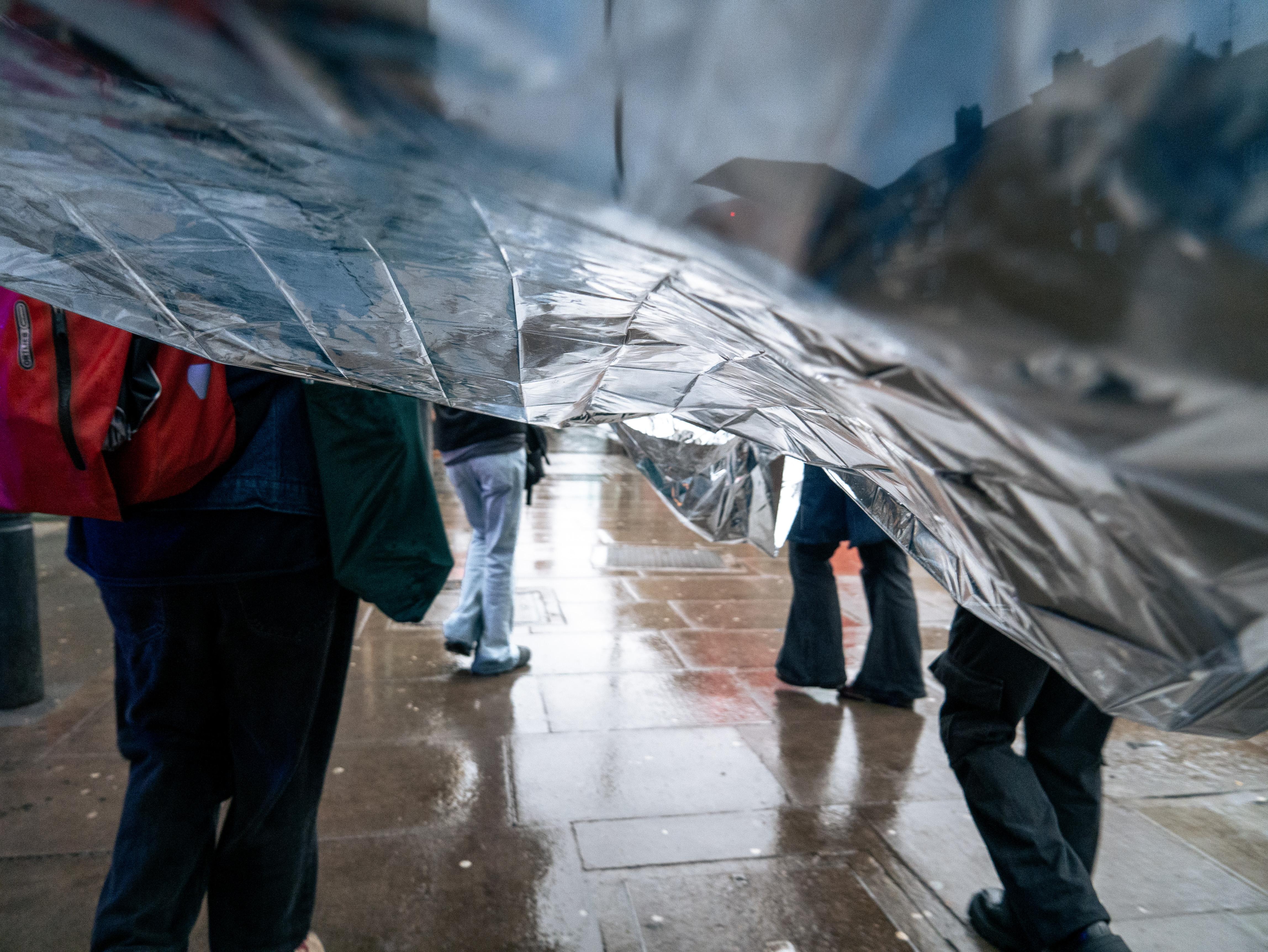A shot from beneath a strip of aluminium foil carried by people through a rainy street.