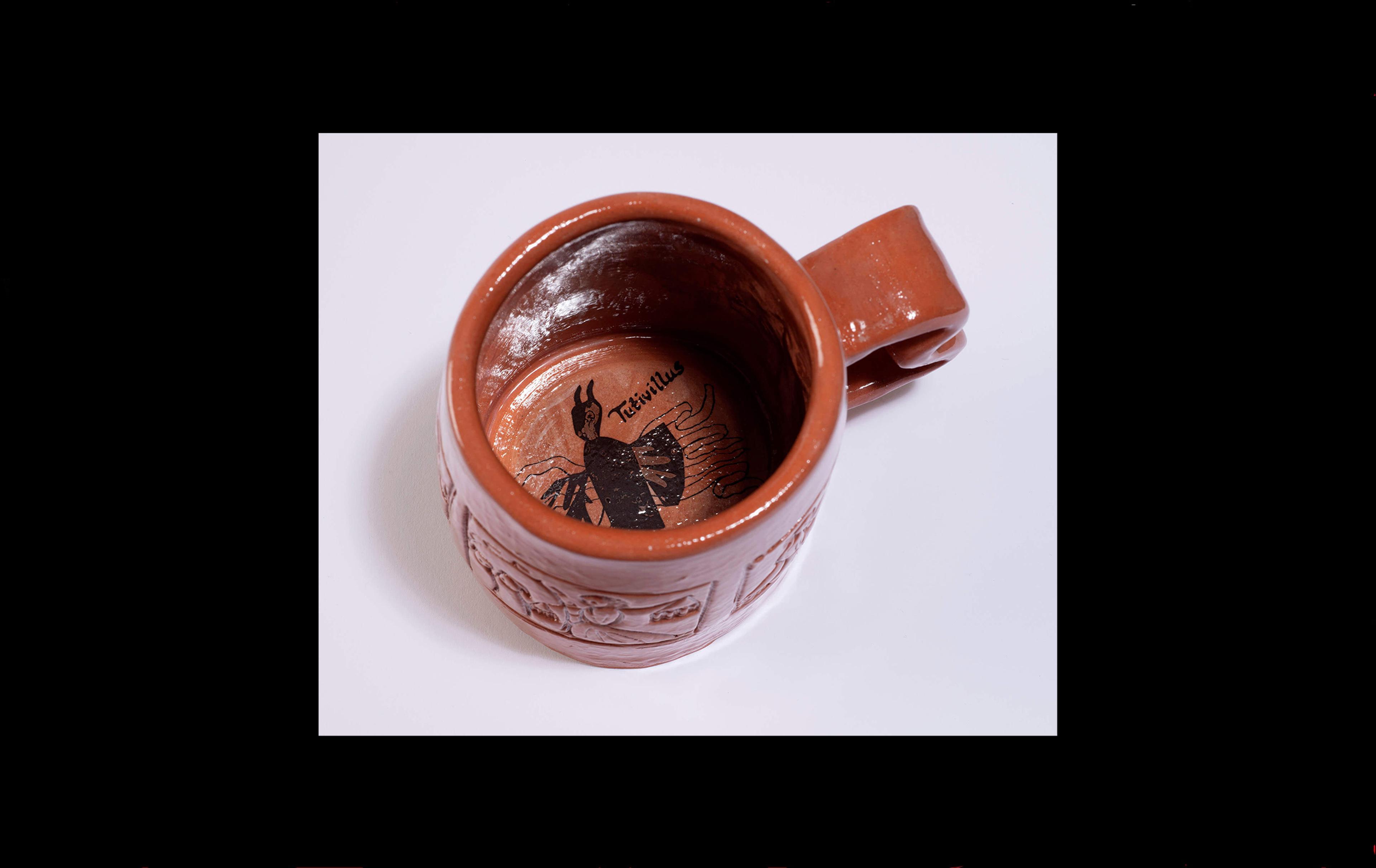 Photograph of red mug seen from above with a black image of a horned and winged figure inside