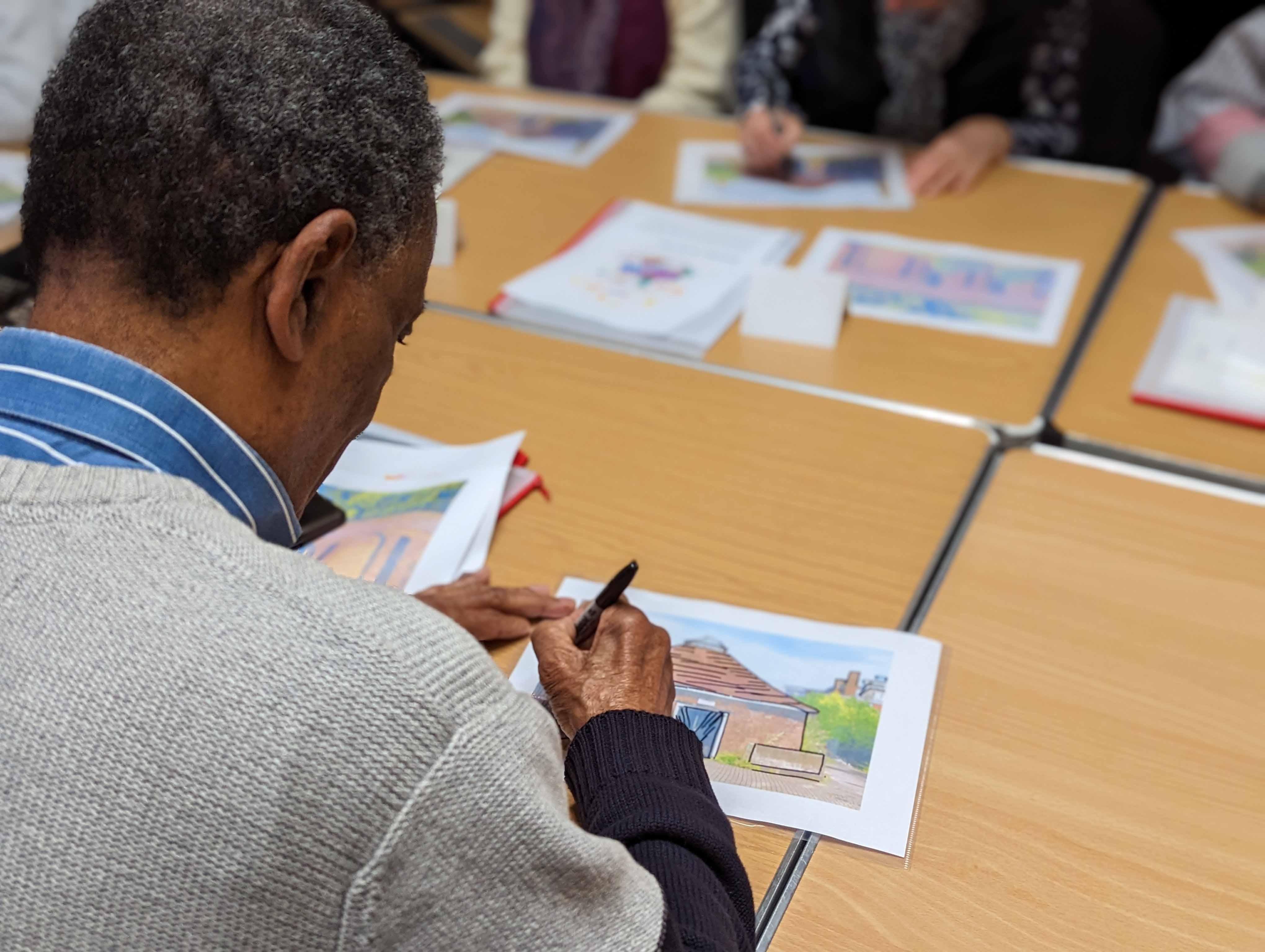 A person at a desk tracing the outline of a building with a pen onto tracing paper.