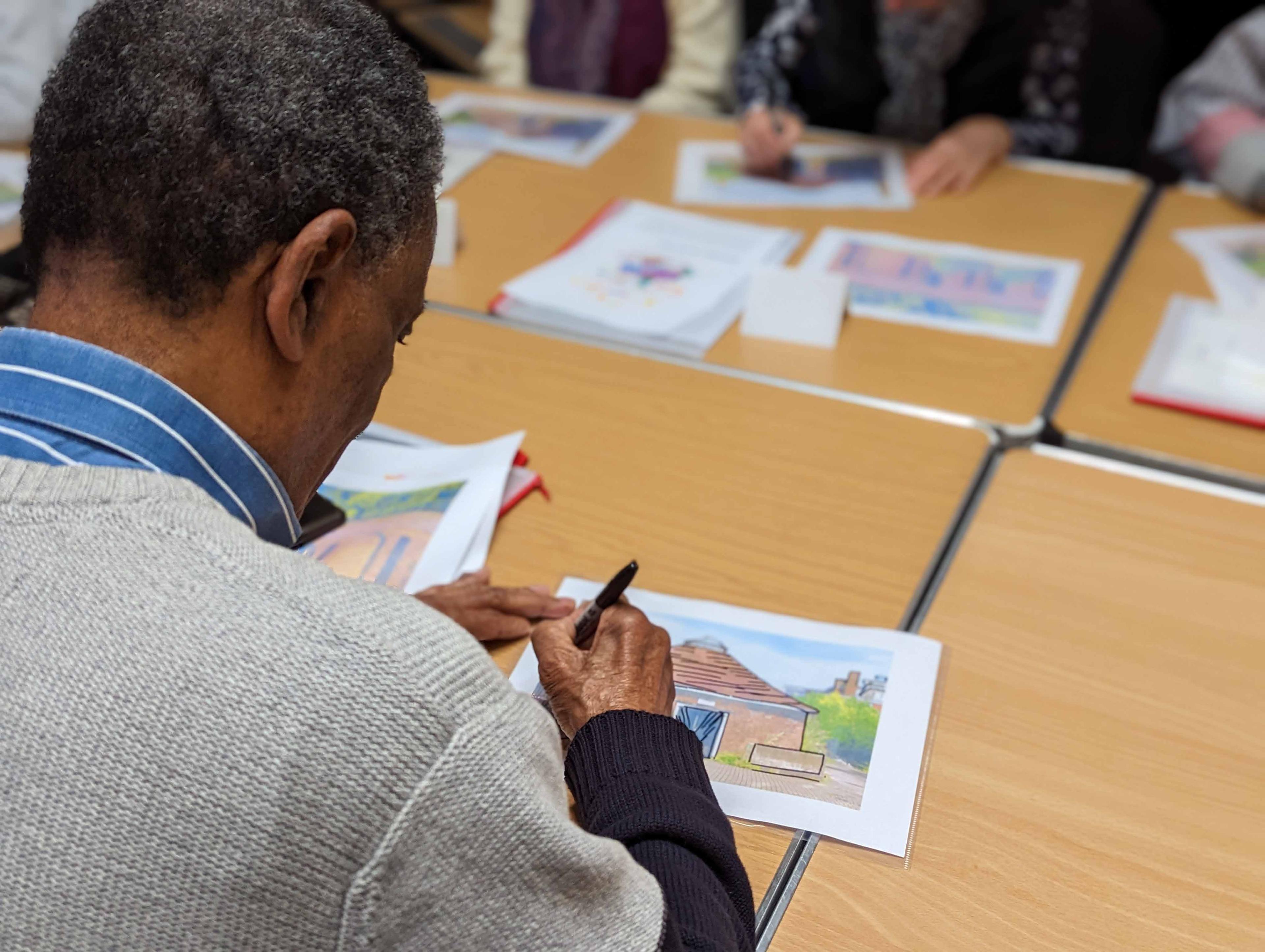 A person at a desk tracing the outline of a building with a pen onto tracing paper.