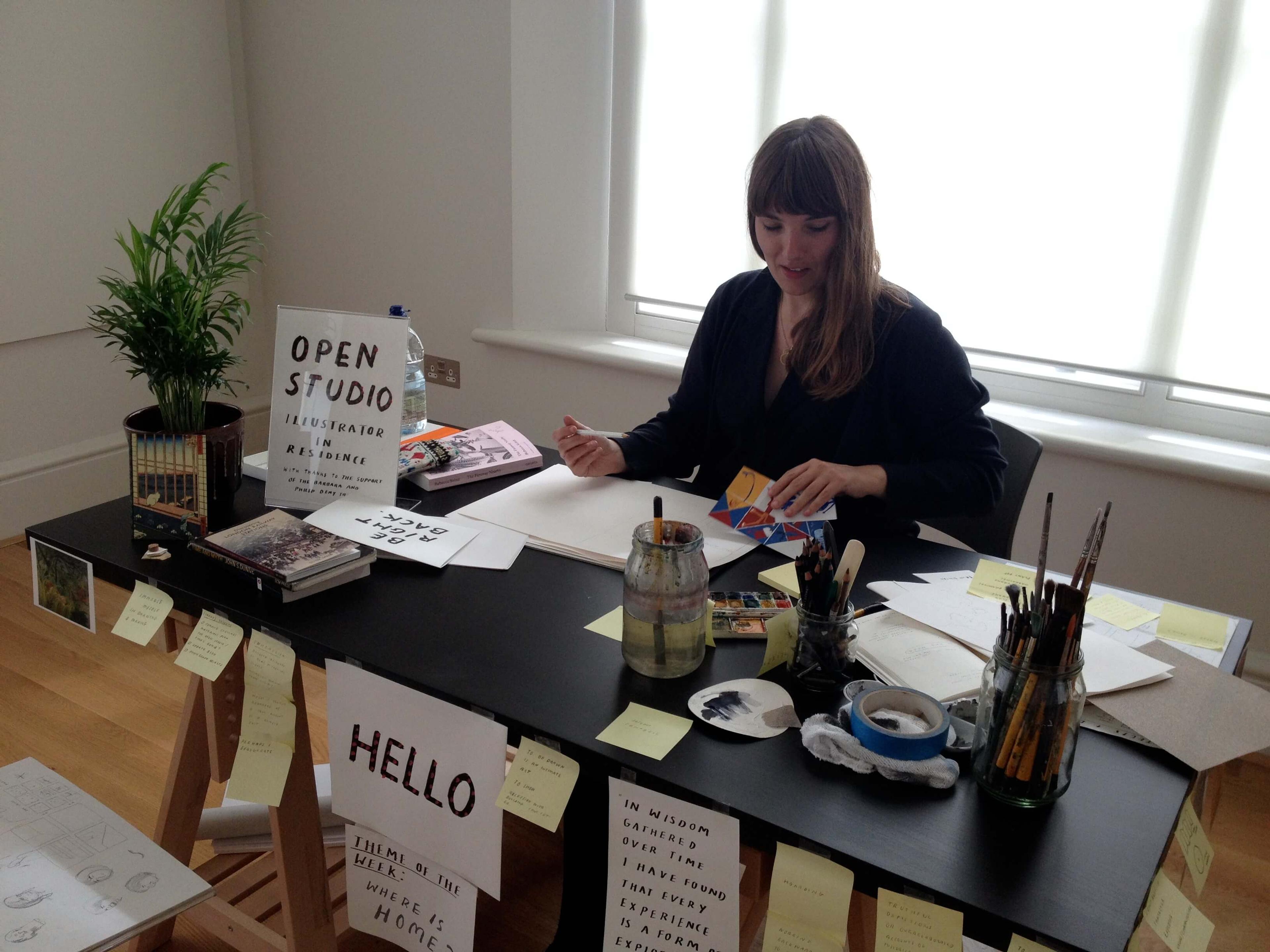 A person is sitting at a desk covered in signs. They have art materials.