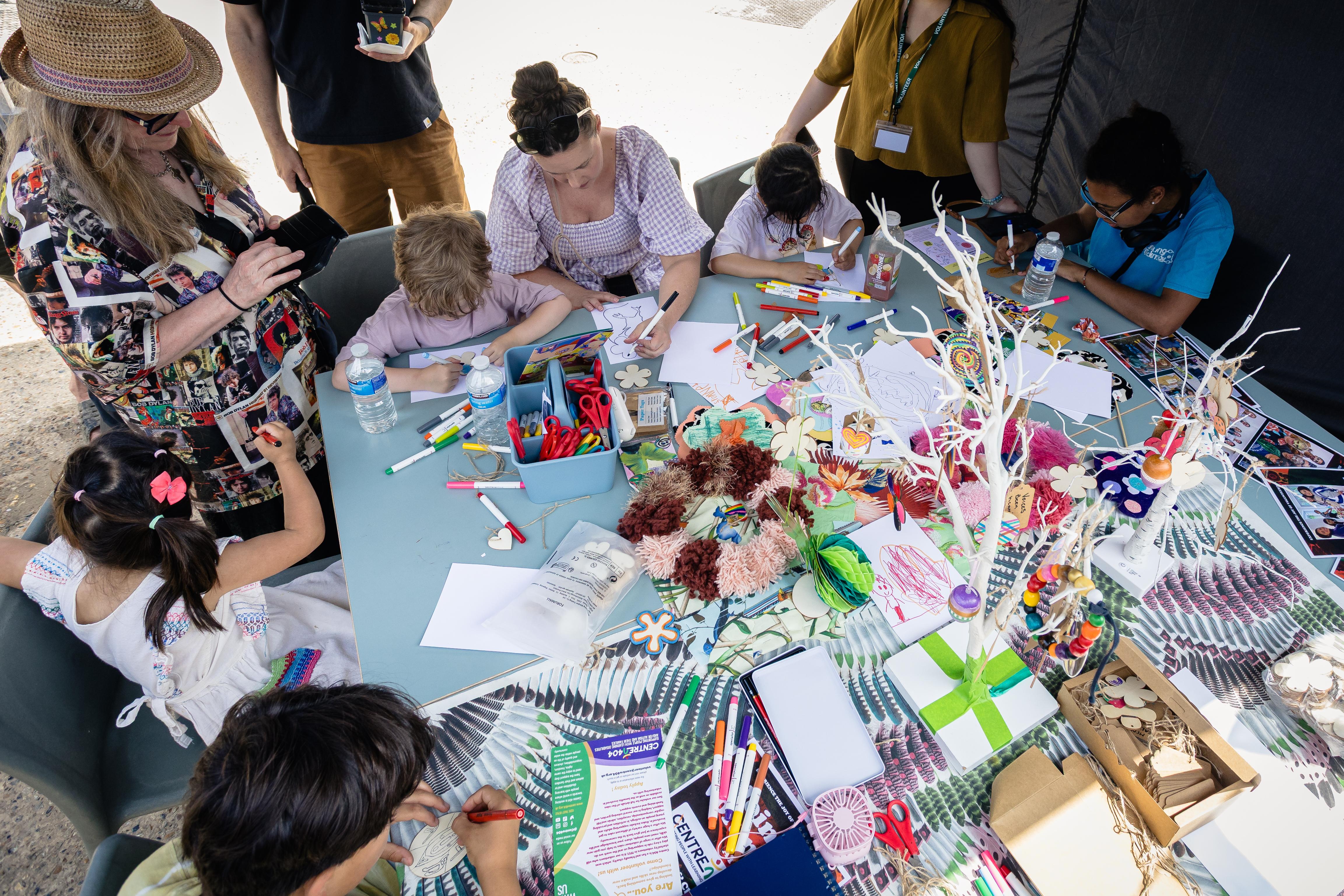 A photo of families sat around a messy table participating in illustration activities using a range a materials and resources.