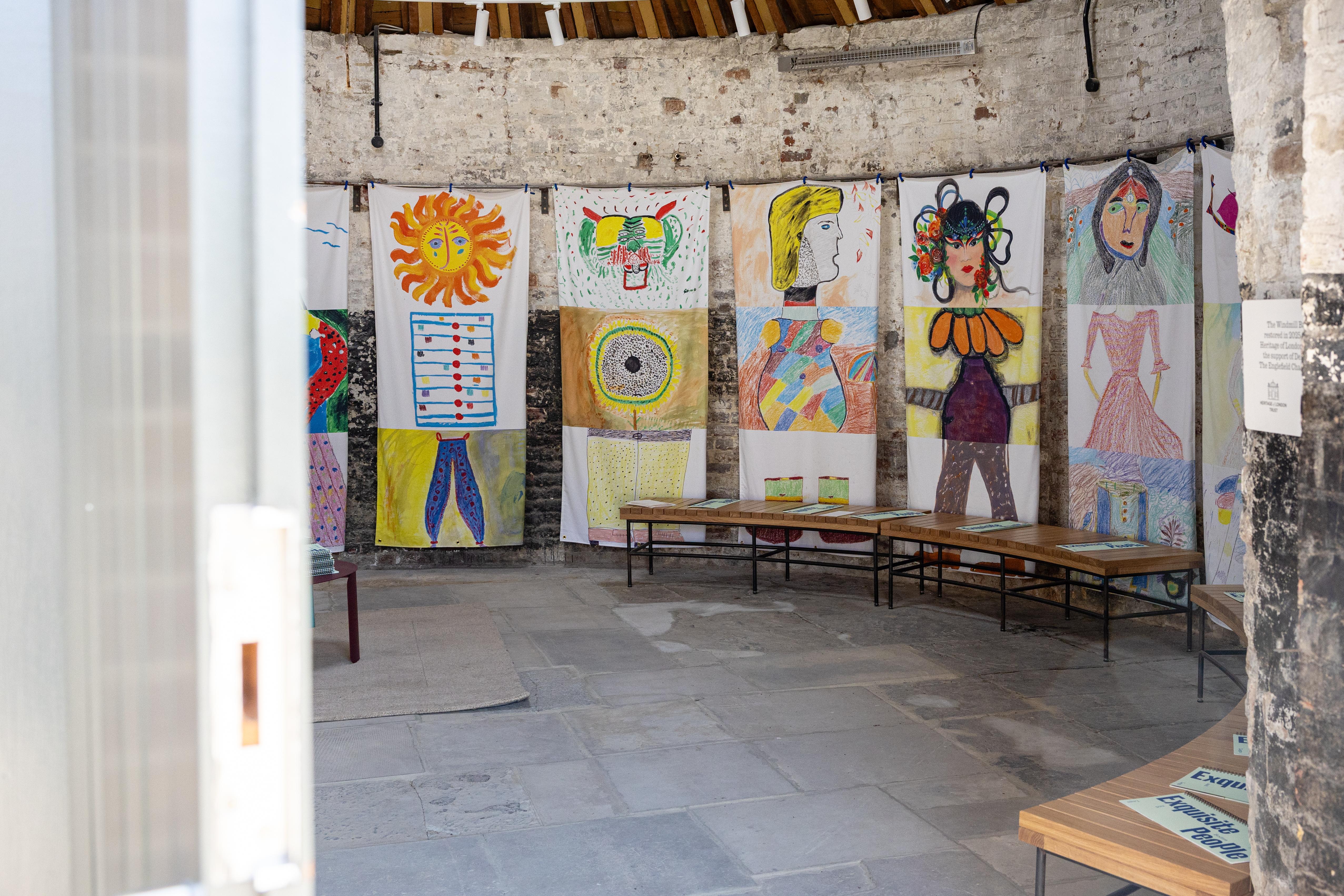 The interior of a round building with hanging fabrics each featuring an assembled head, body and neck drawn in different styles.