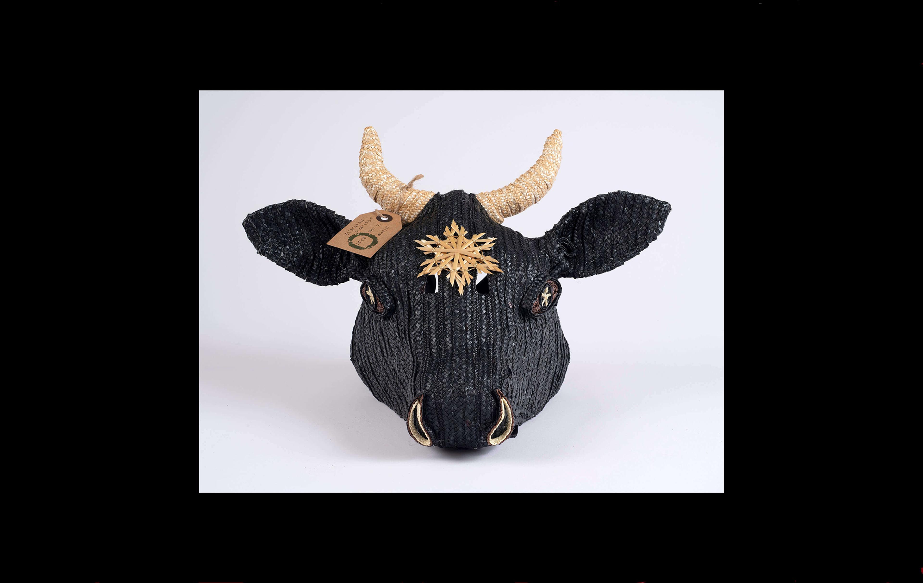 Photograph of a cow's head made with black straw and with a yellow straw woven star on its forehead