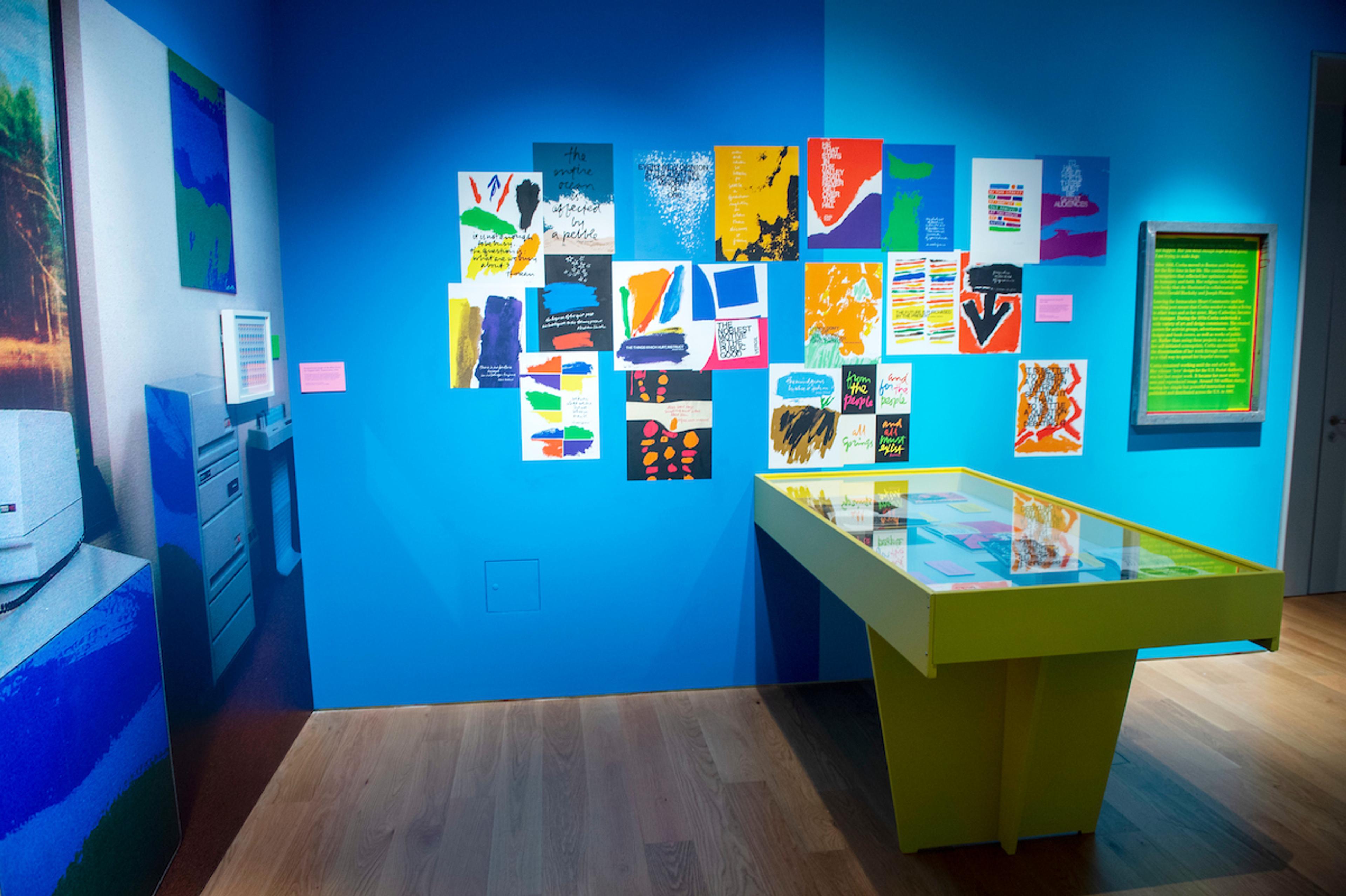 Photograph from the exhibition featuring a blue wall and display cases with illustrations on display