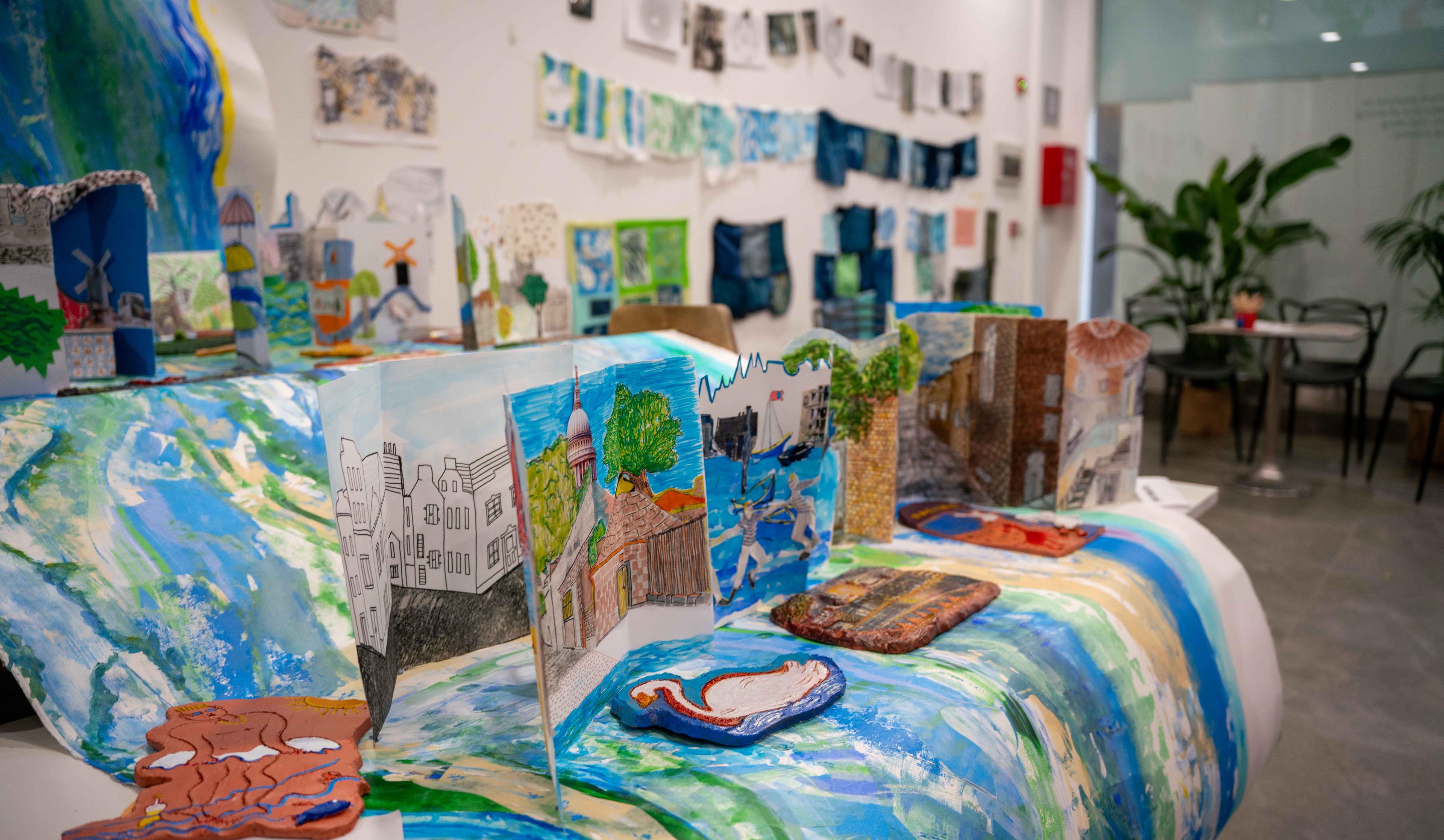 Photograph of the inside of a display of illustration, with a large paper river on display with ceramics and paper sculptures sitting on top of the paper river.