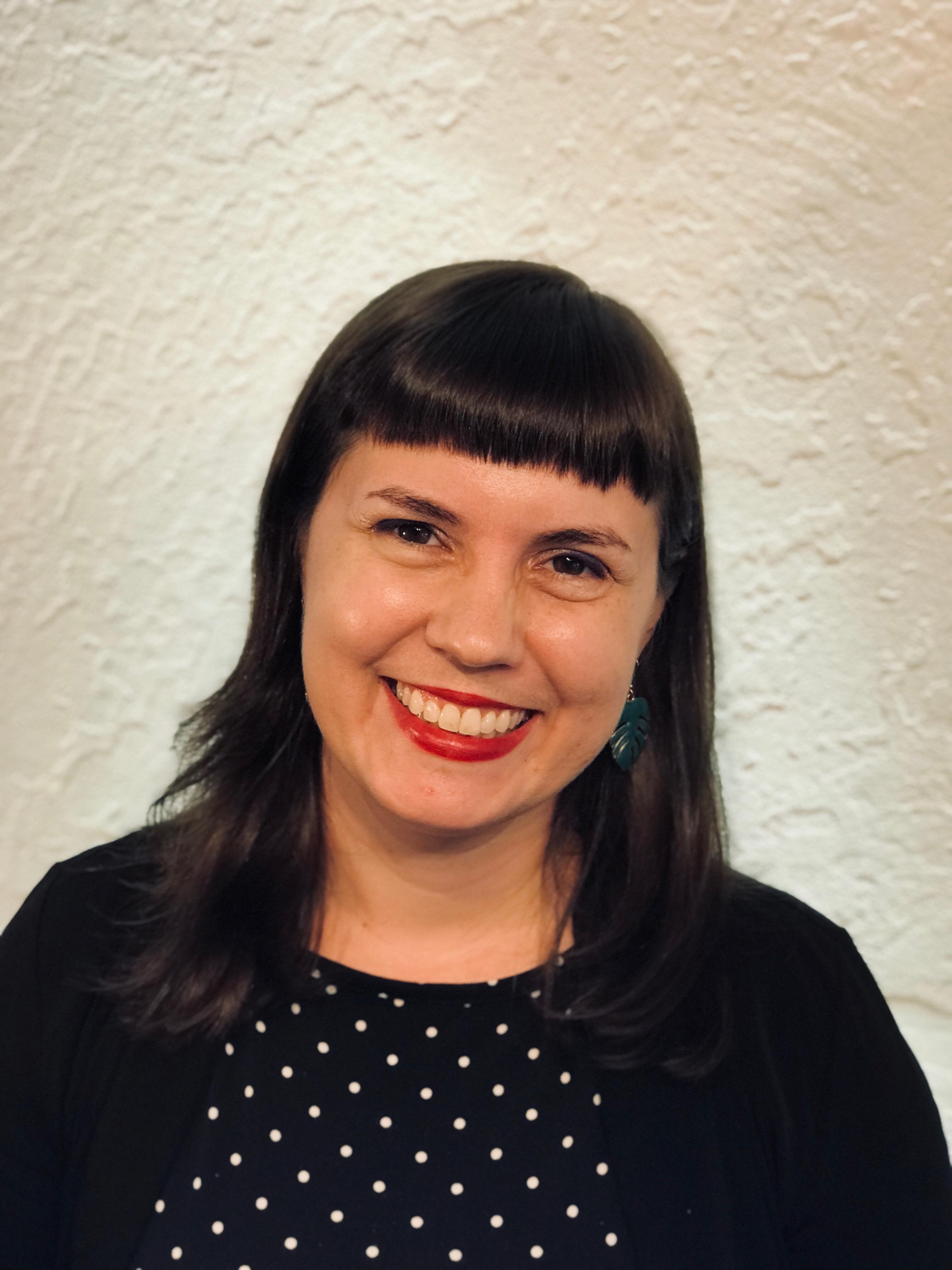 A woman with short brown hair wearing a black polka dot dress, smiling at the camera.