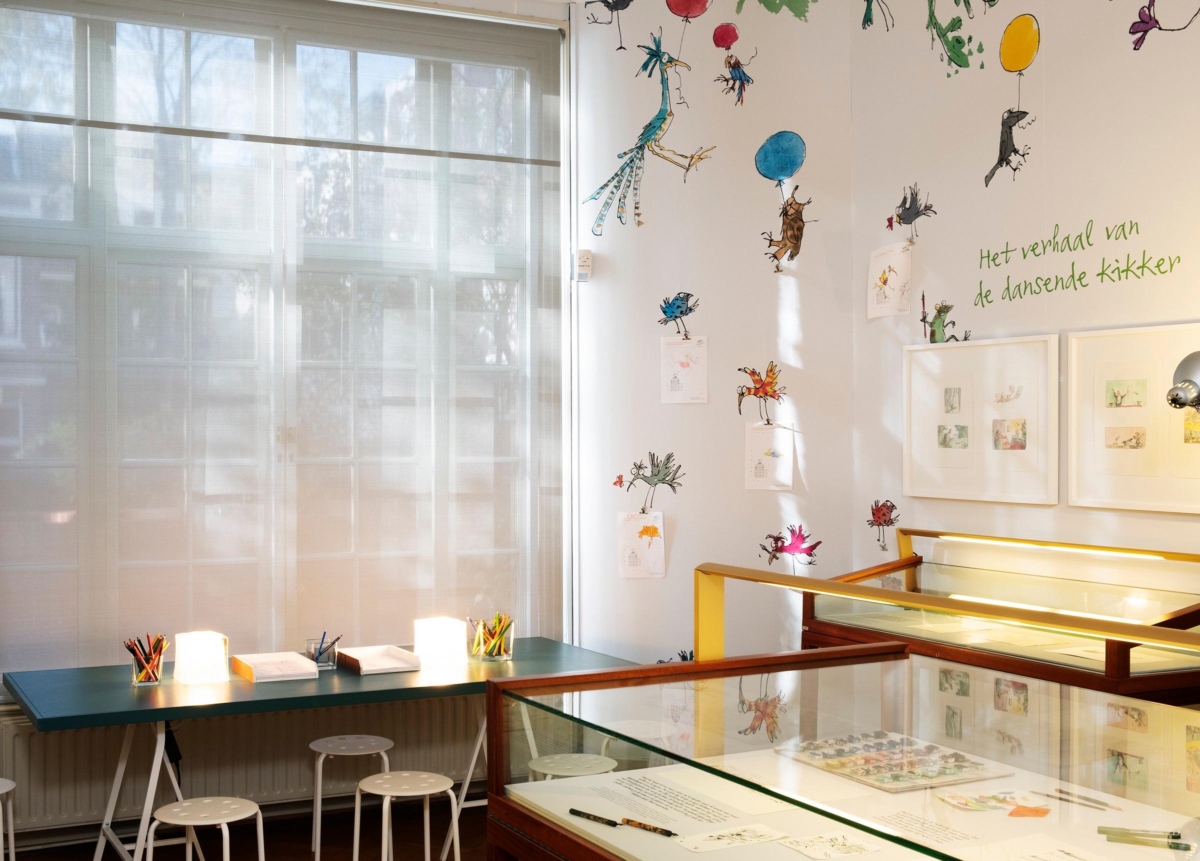 Exhibition photograph showing activity table and display cases with framed artwork on the wall 