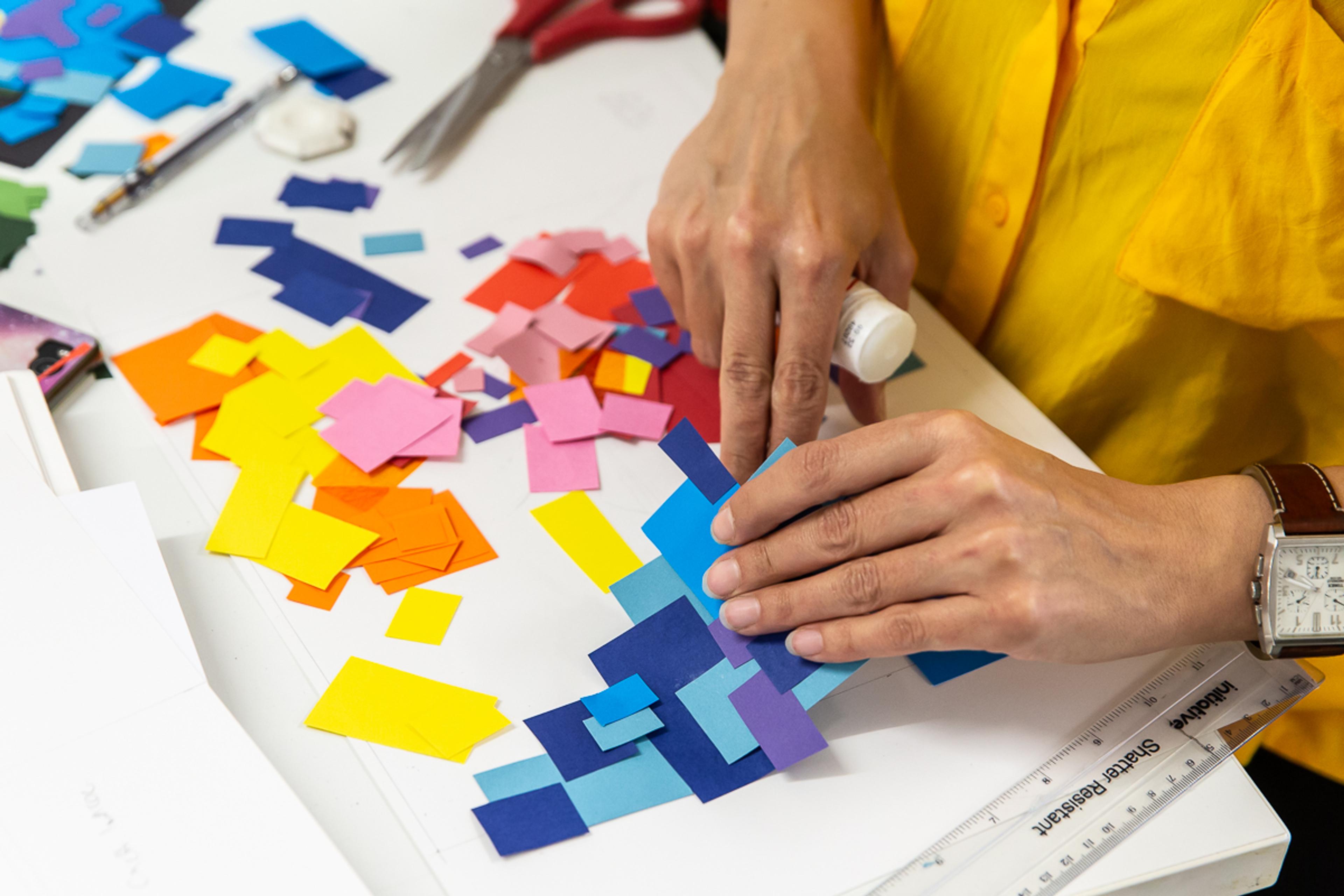 Photograph of hands making a collage from coloured paper squares