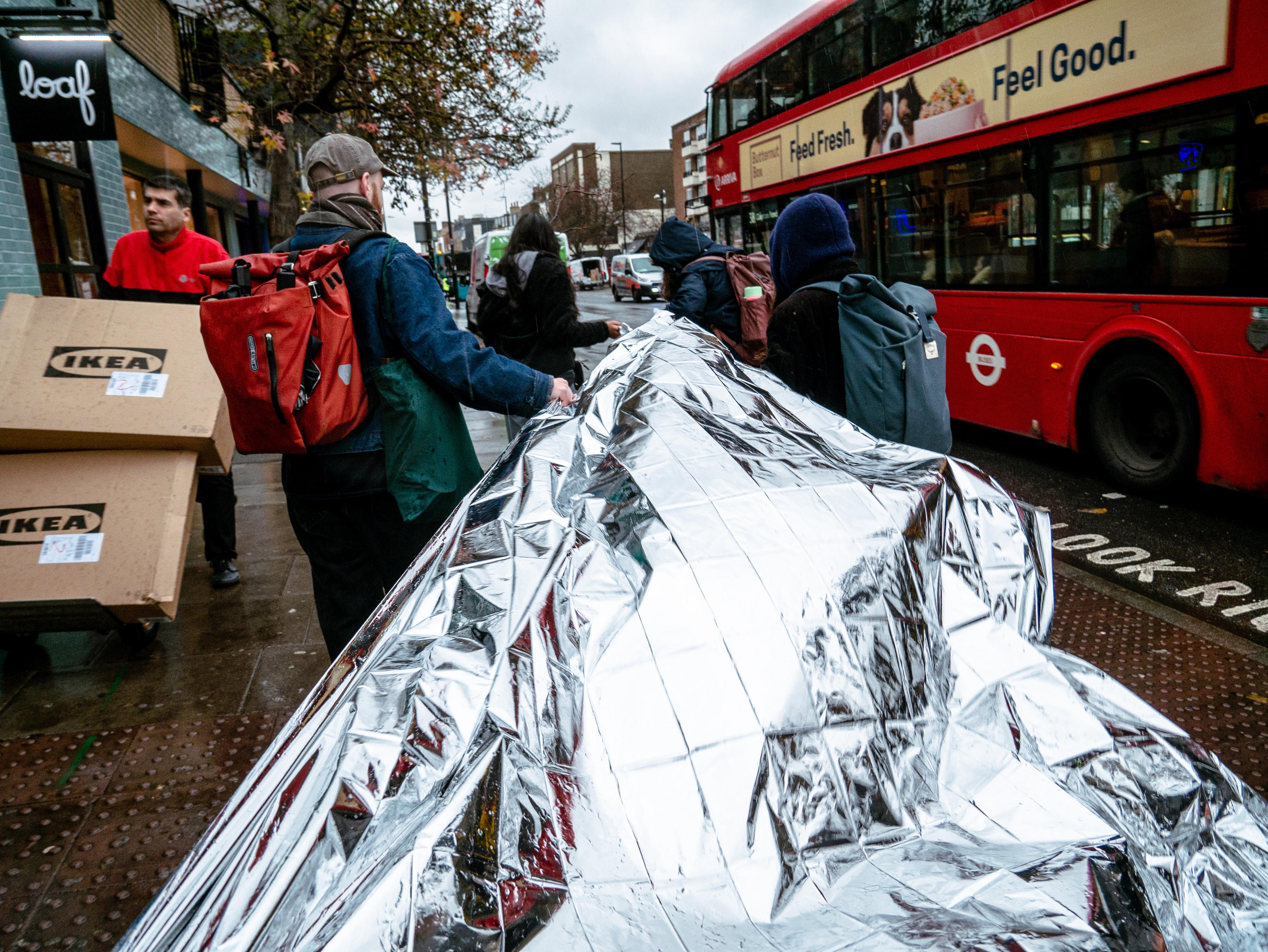 A group of people pull a strip of foil down a rainy road in London.