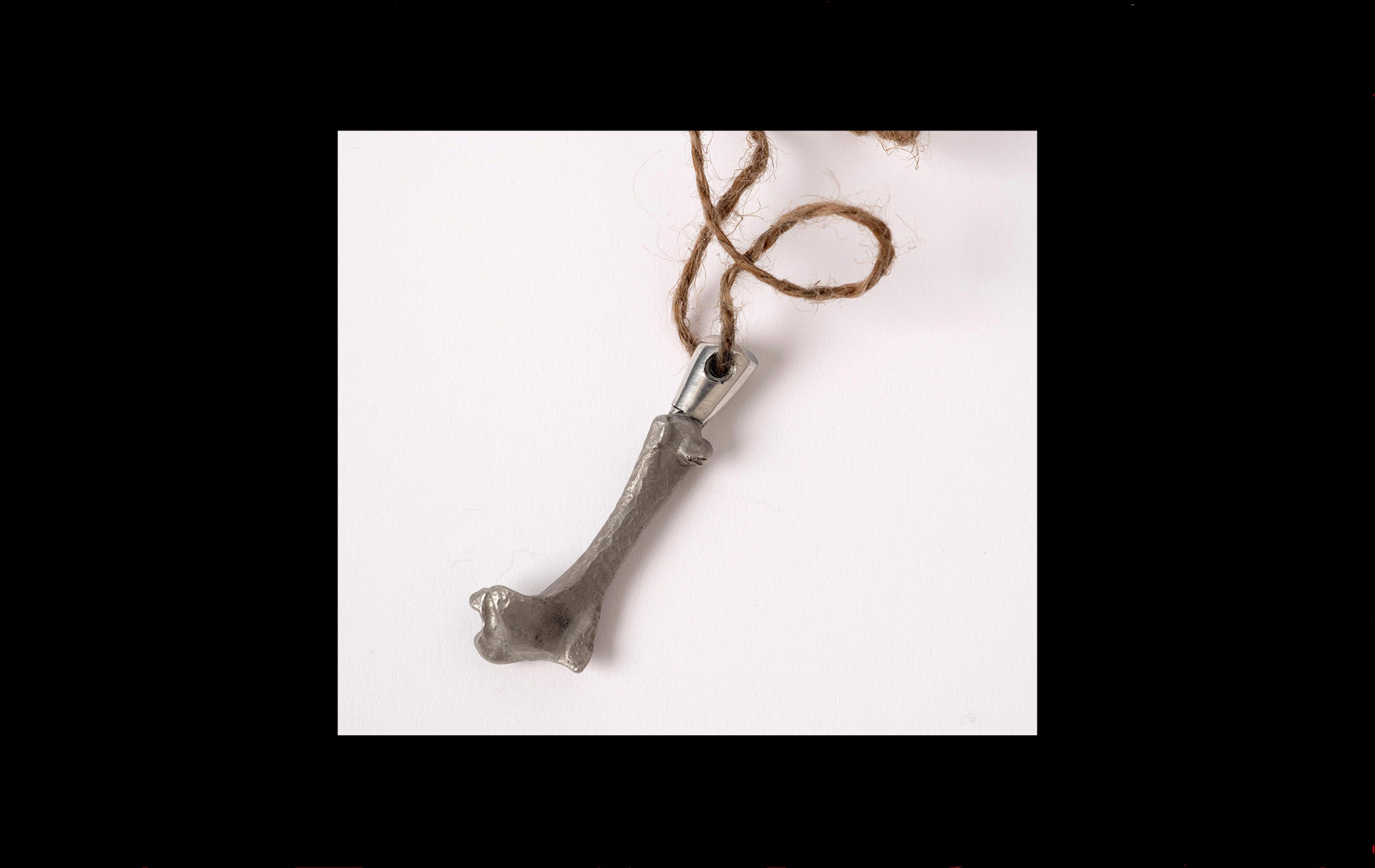 Photograph of a bone cast in pewter with a brown string threaded through the top