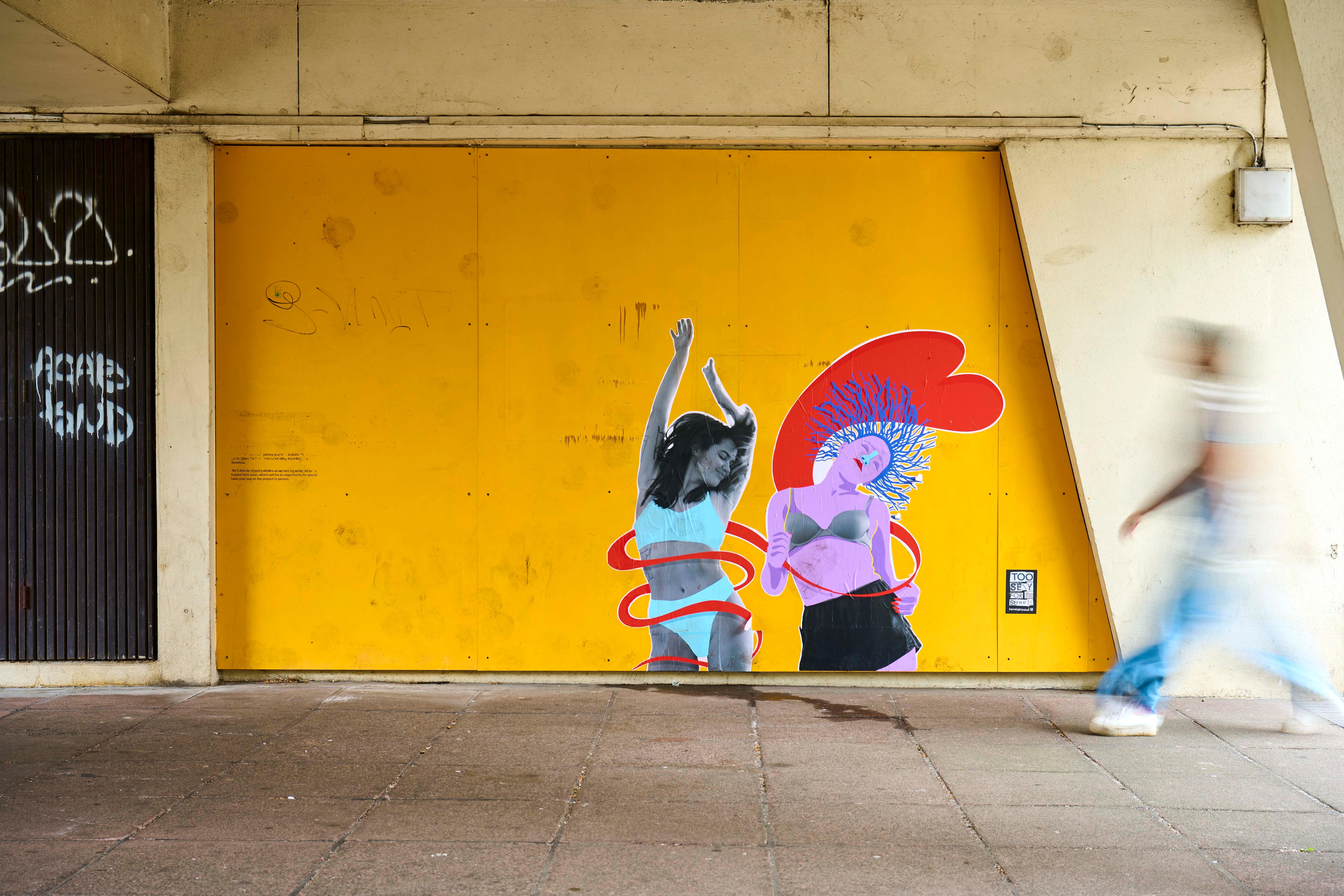 A mural with two women moving against a yellow background in an urban environment.