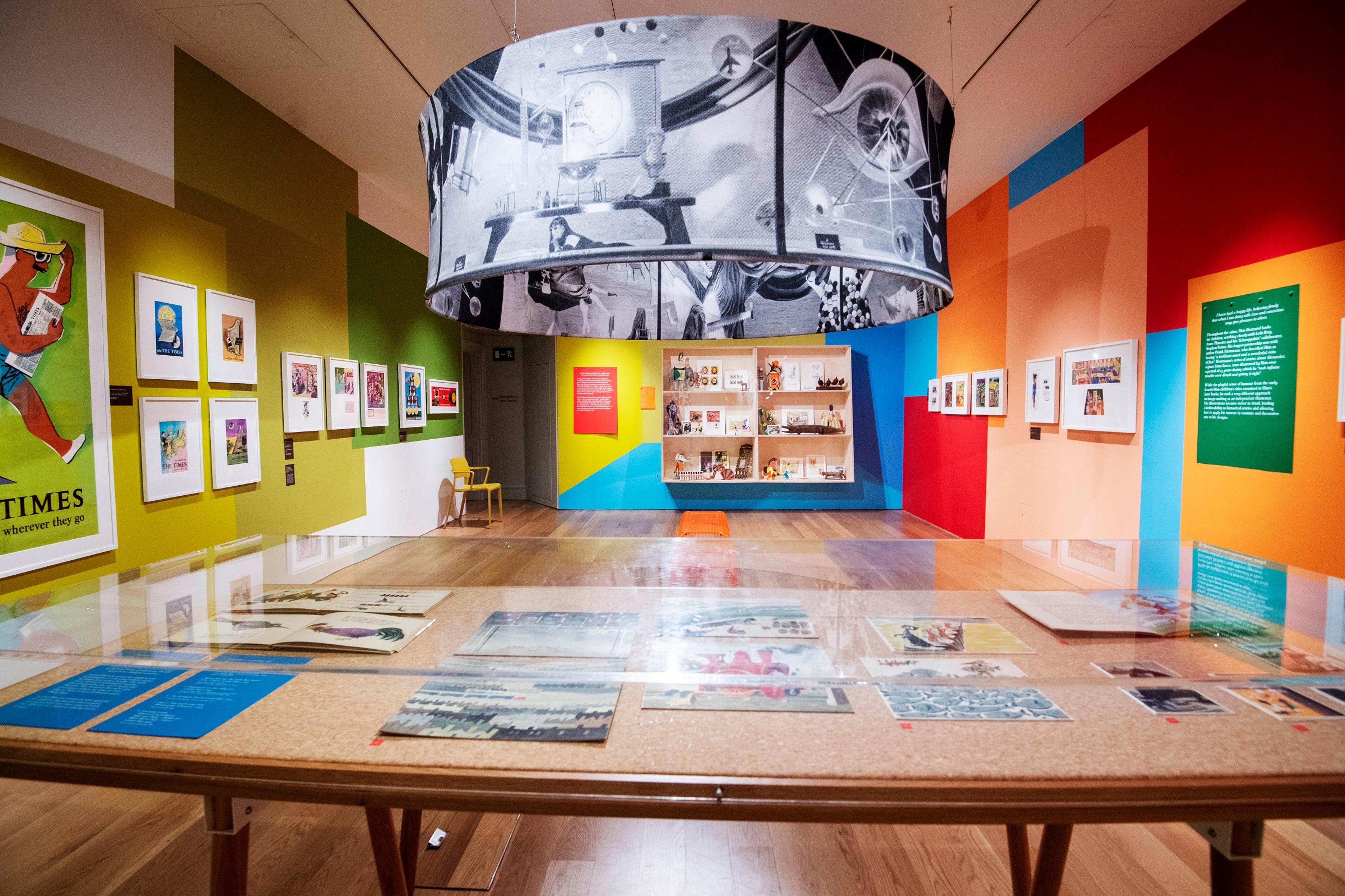Framed artwork on brightly painted walls, with suspended cylinder displaying black and white photographs