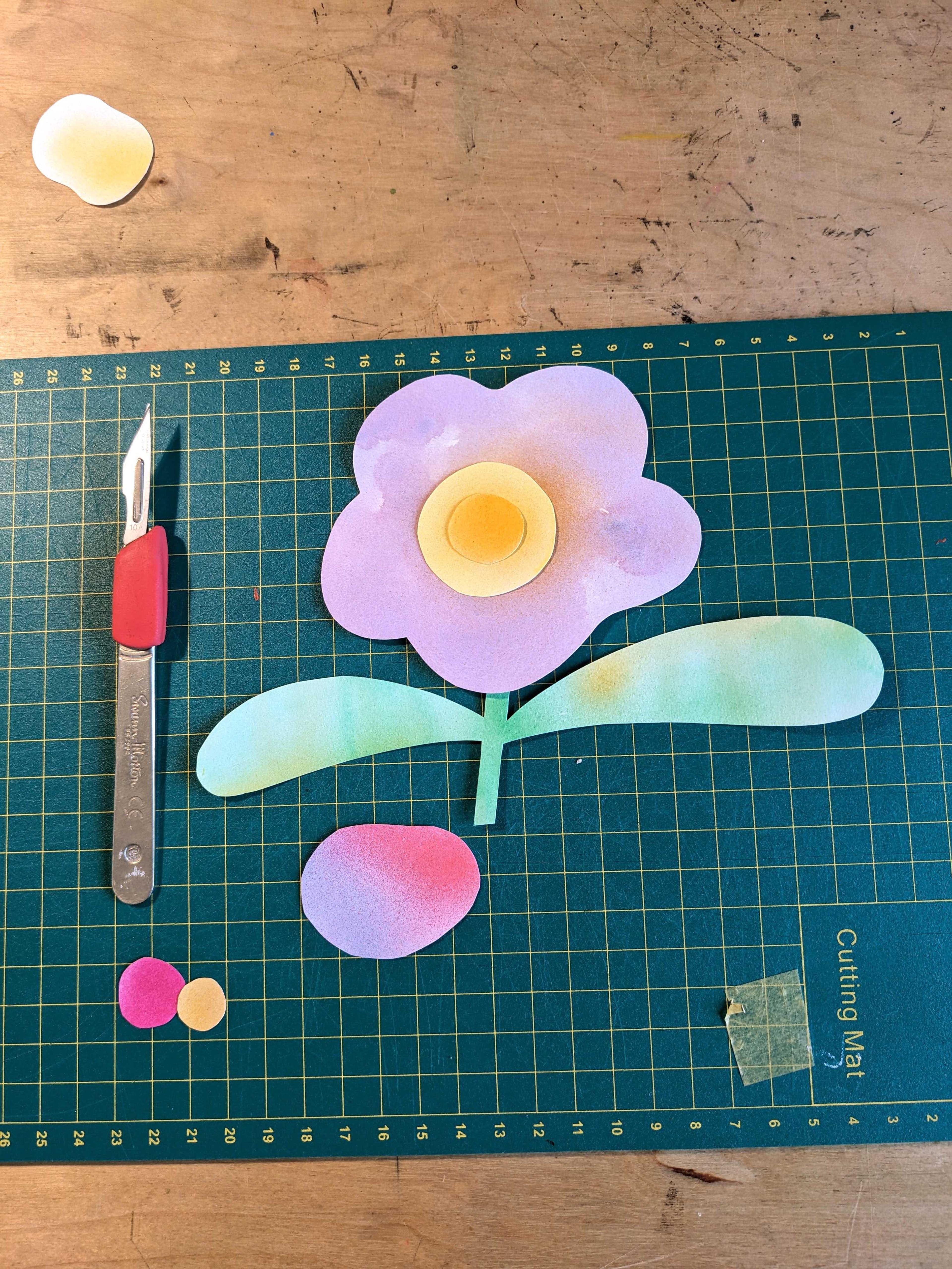 Illustration of a flower with leaves on a cutting mat with a scalpel.