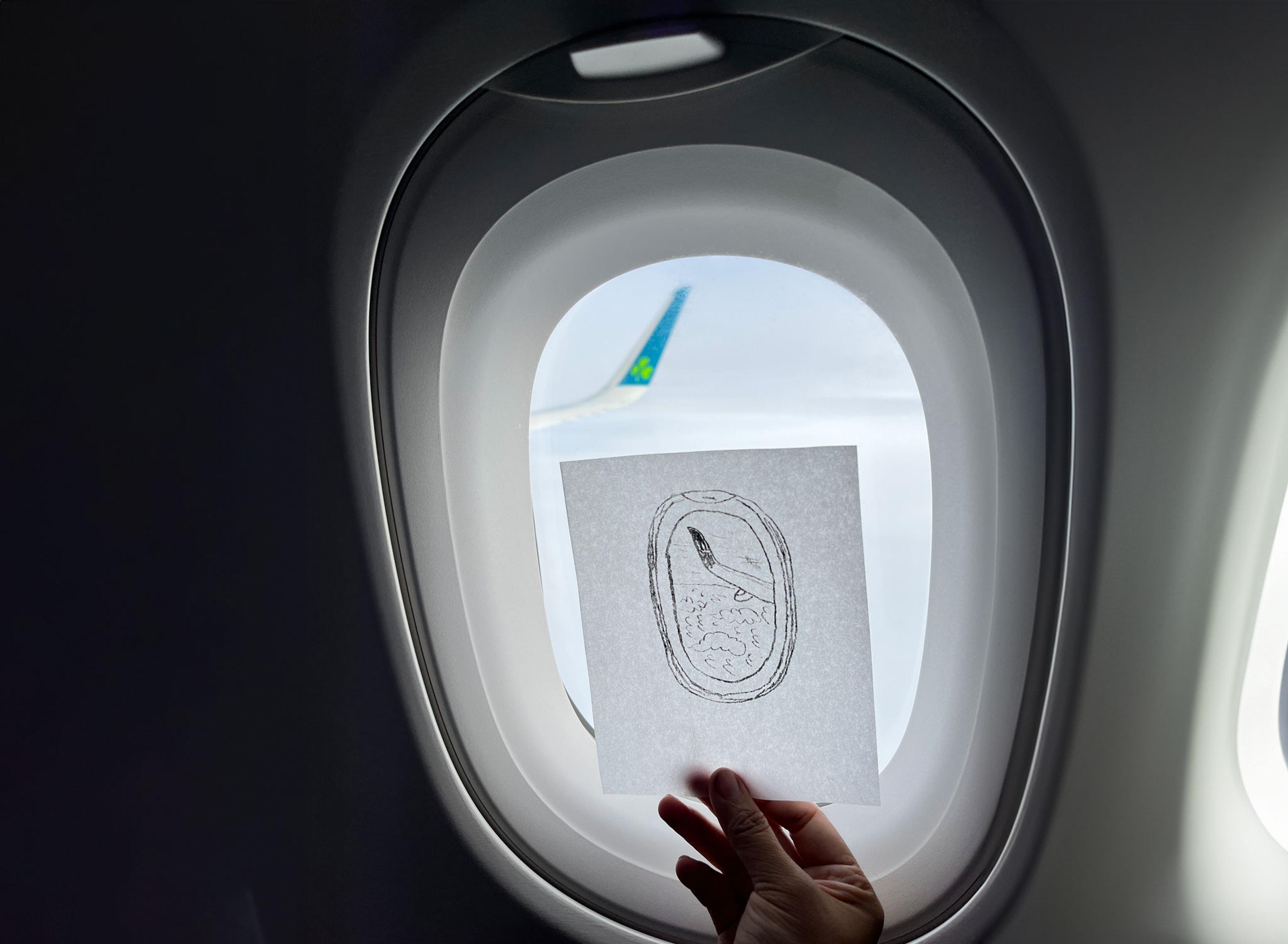 A drawing of an airplane widows with clouds and the an airplane wing being held up against an airplane window.