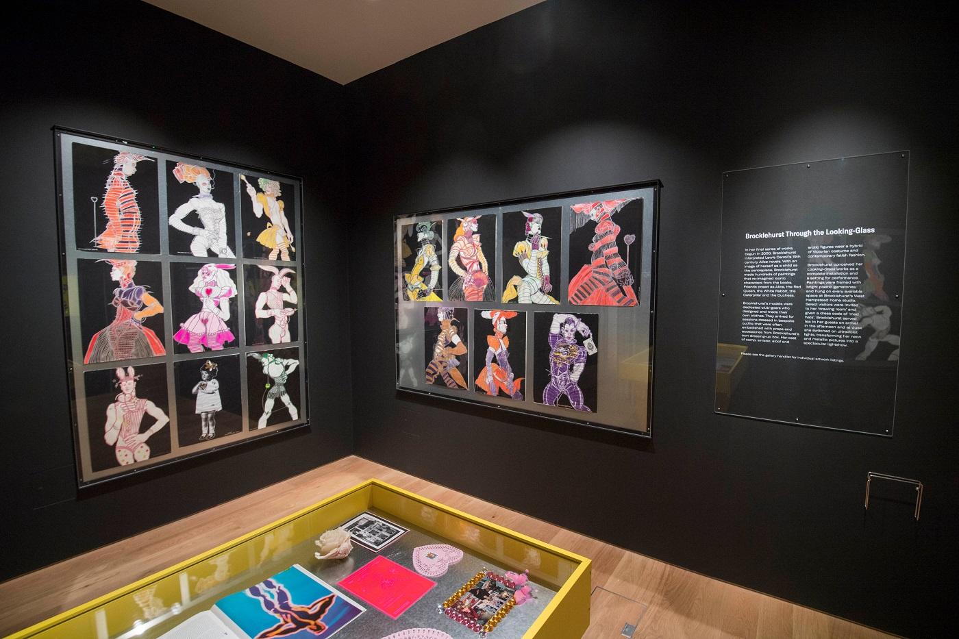 Photograph of large drawings hung on silver sheet metal on black gallery walls