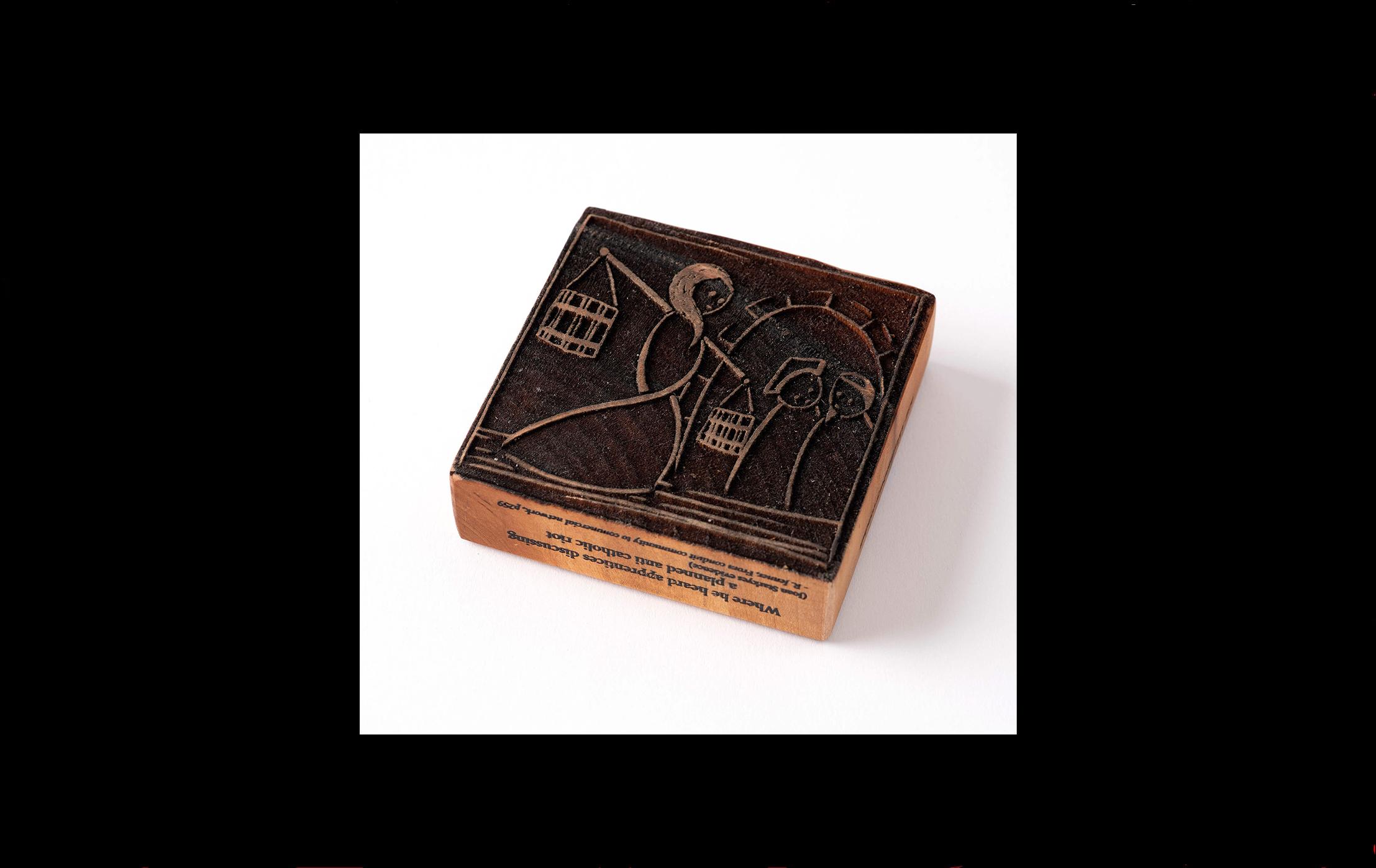 Wood block with an image of a woman carrying two water buckets looking at two people talking under an archway etched into the surface