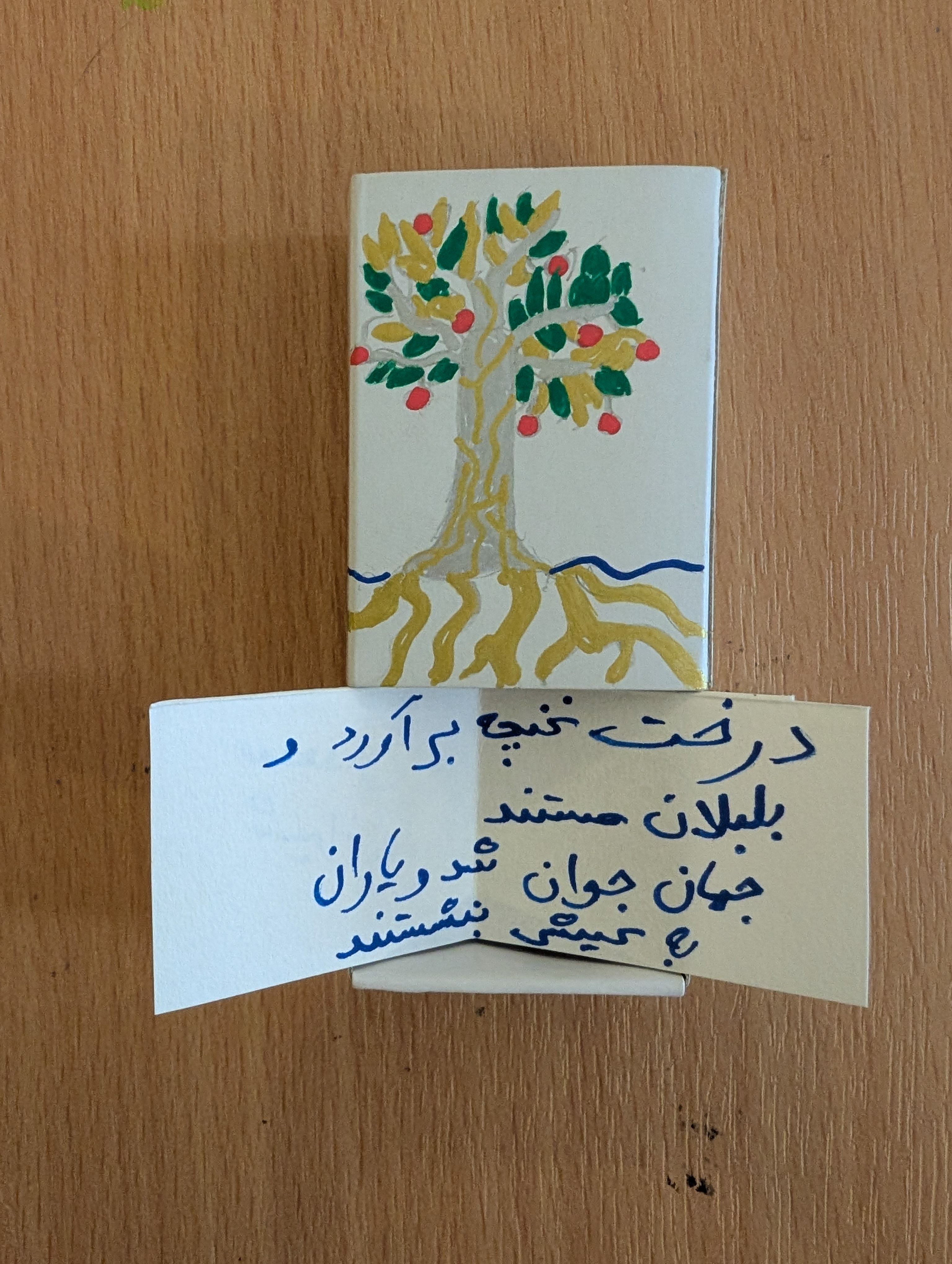 A matchbox with an illustrated tree drawn on the front and a message written in Arabic inside.