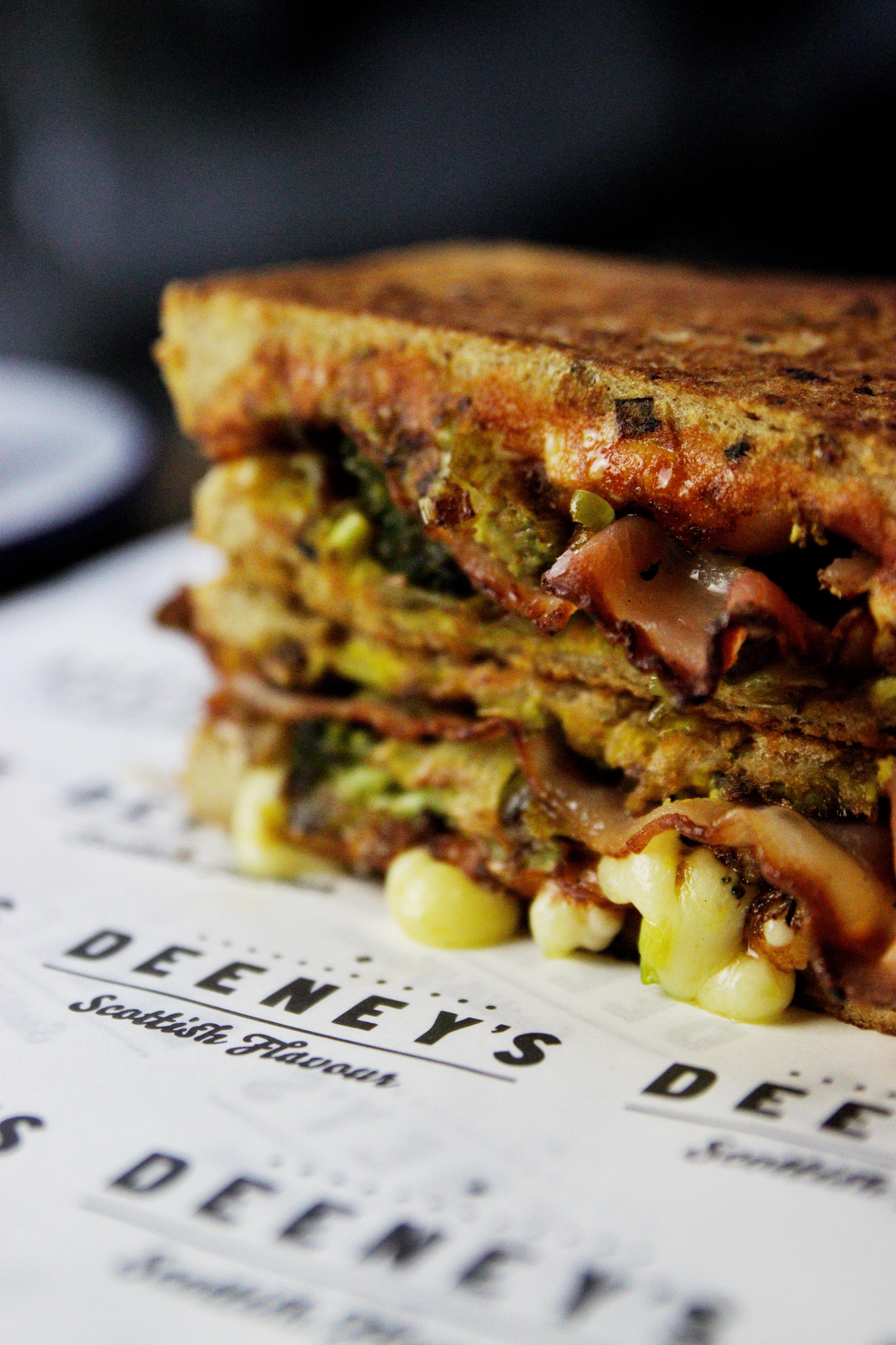 Close-up of a generously-filled toastie oozing with cheese laid on a paper wrapper labelled Deeney's.