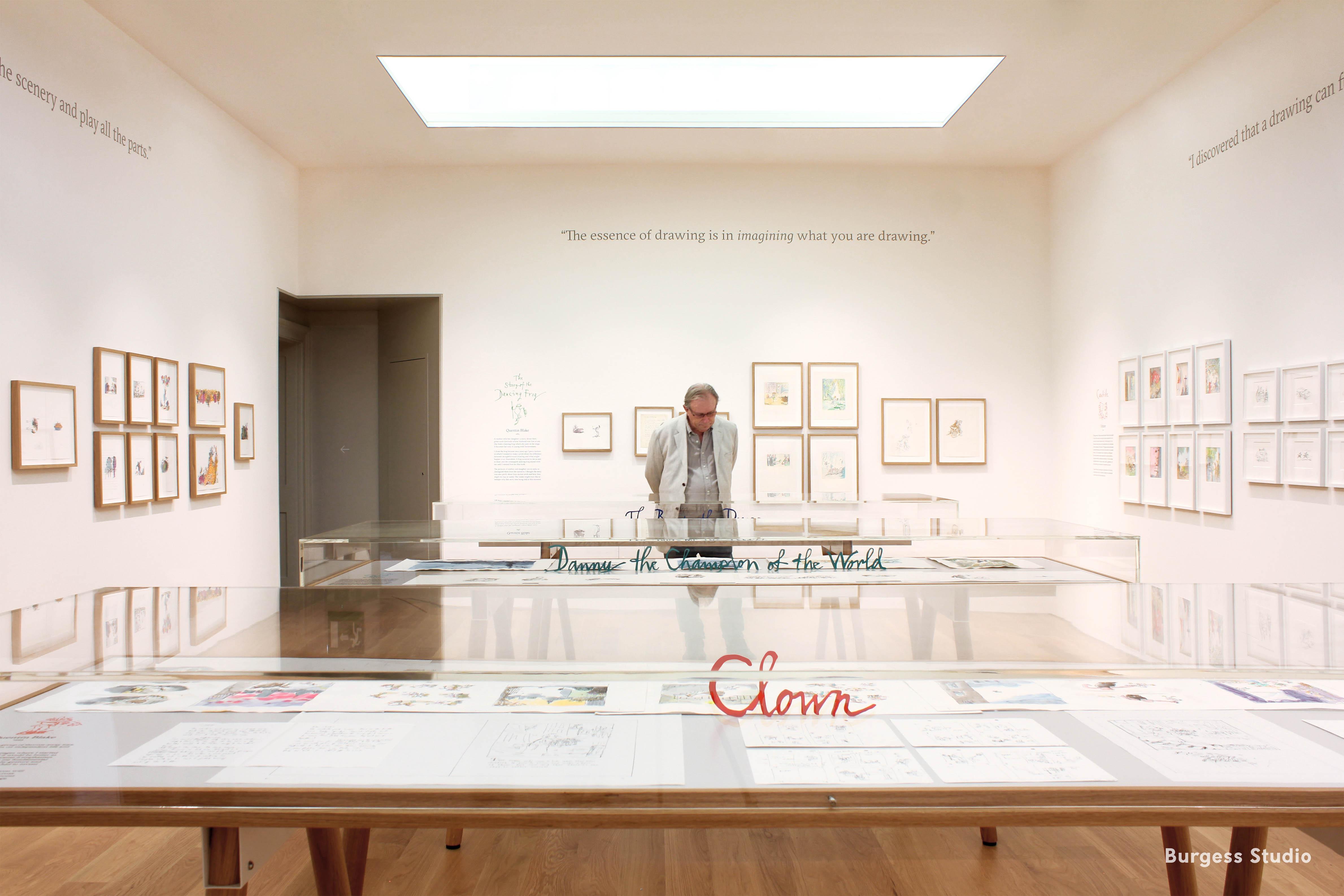 Inside an exhibition space with framed illustrations on the wall and displayed in glass cabinets.