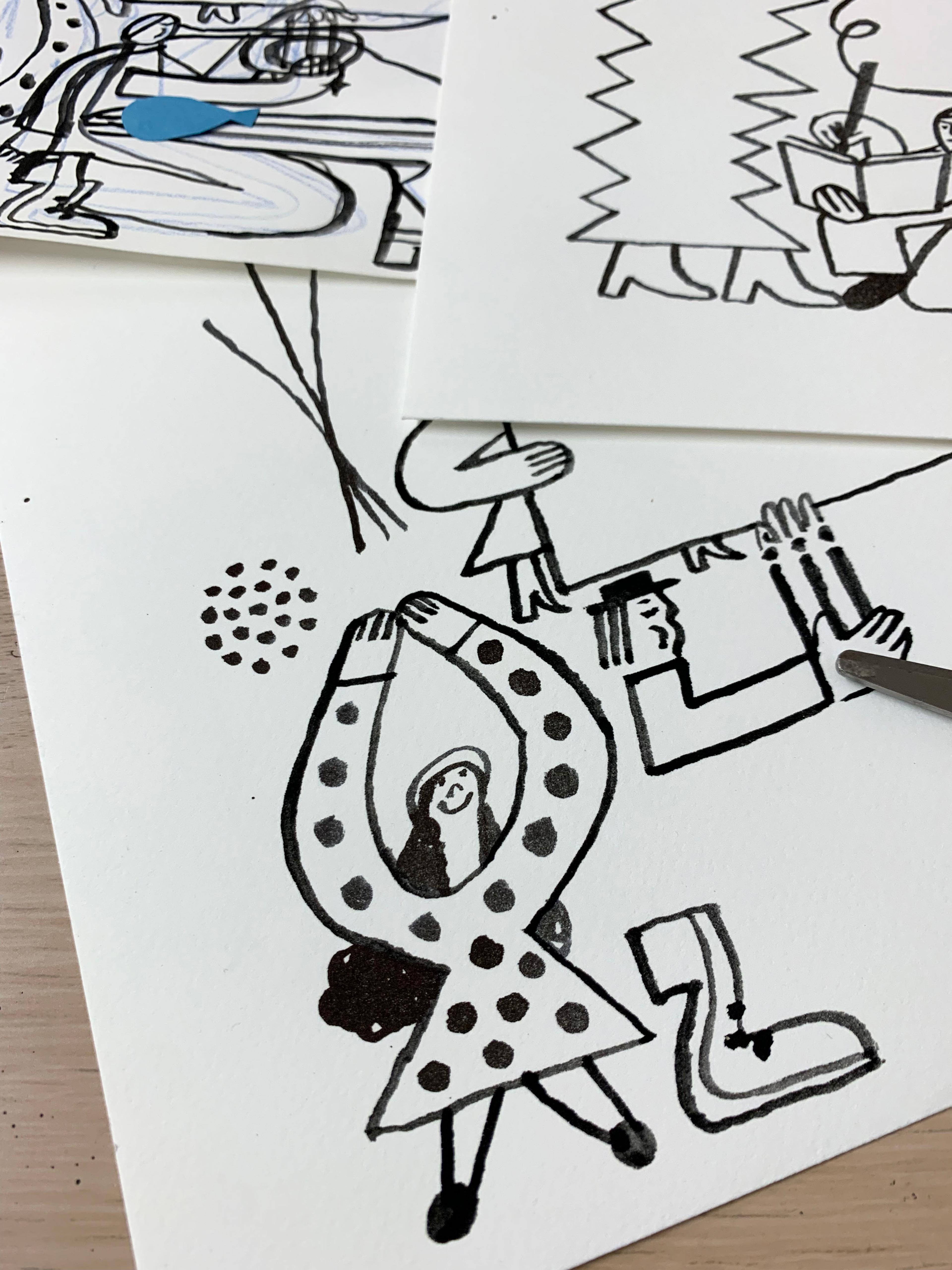 Black and white illustrations on a table surrounded by paint brushes, paper cut outs and scissors.