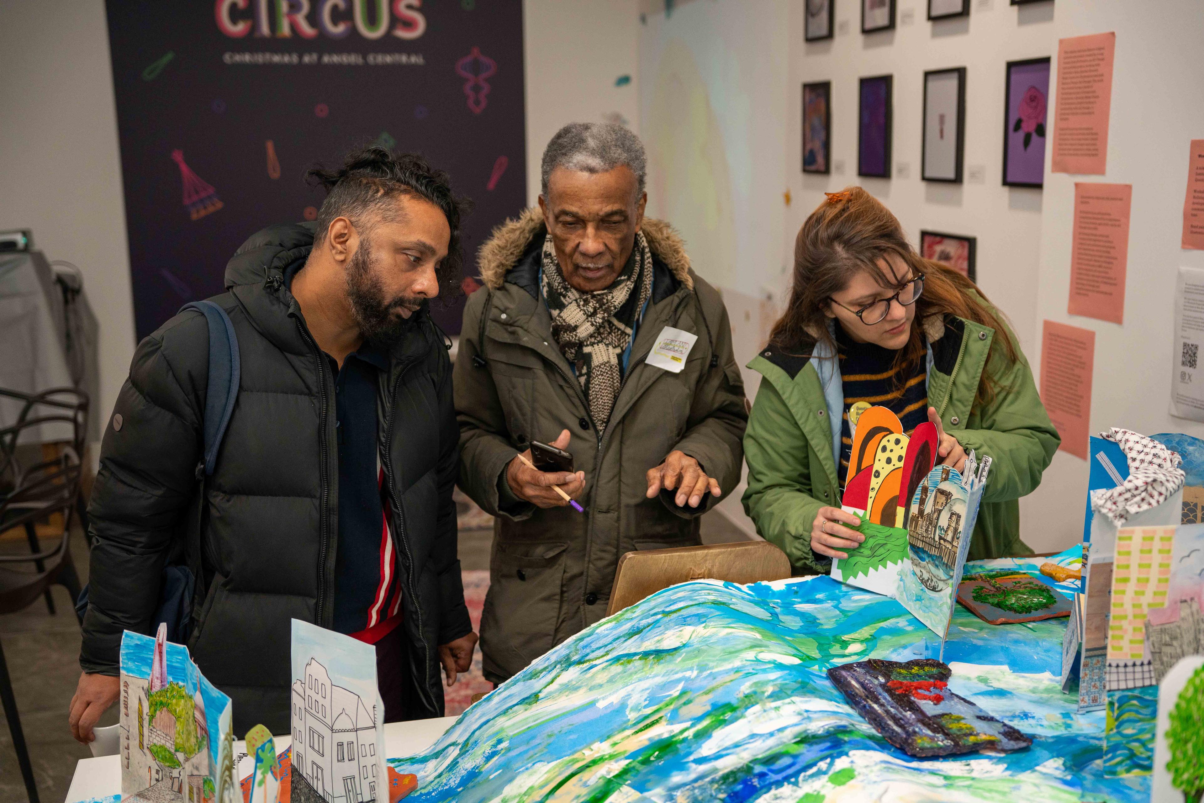 Three people look at an exhibition of illustration and sculpture.