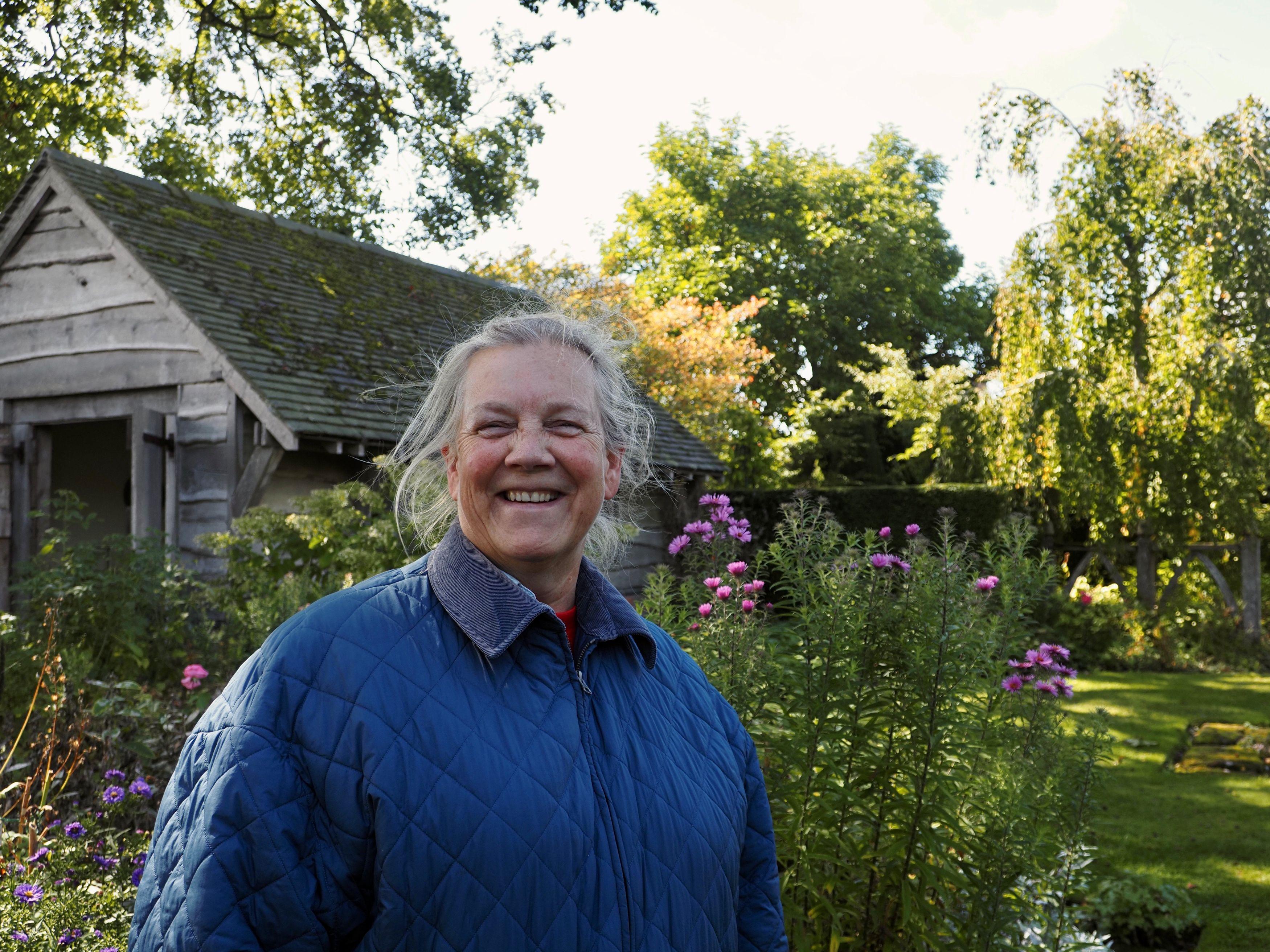A woman smiles at the camera in front of a blooming garden