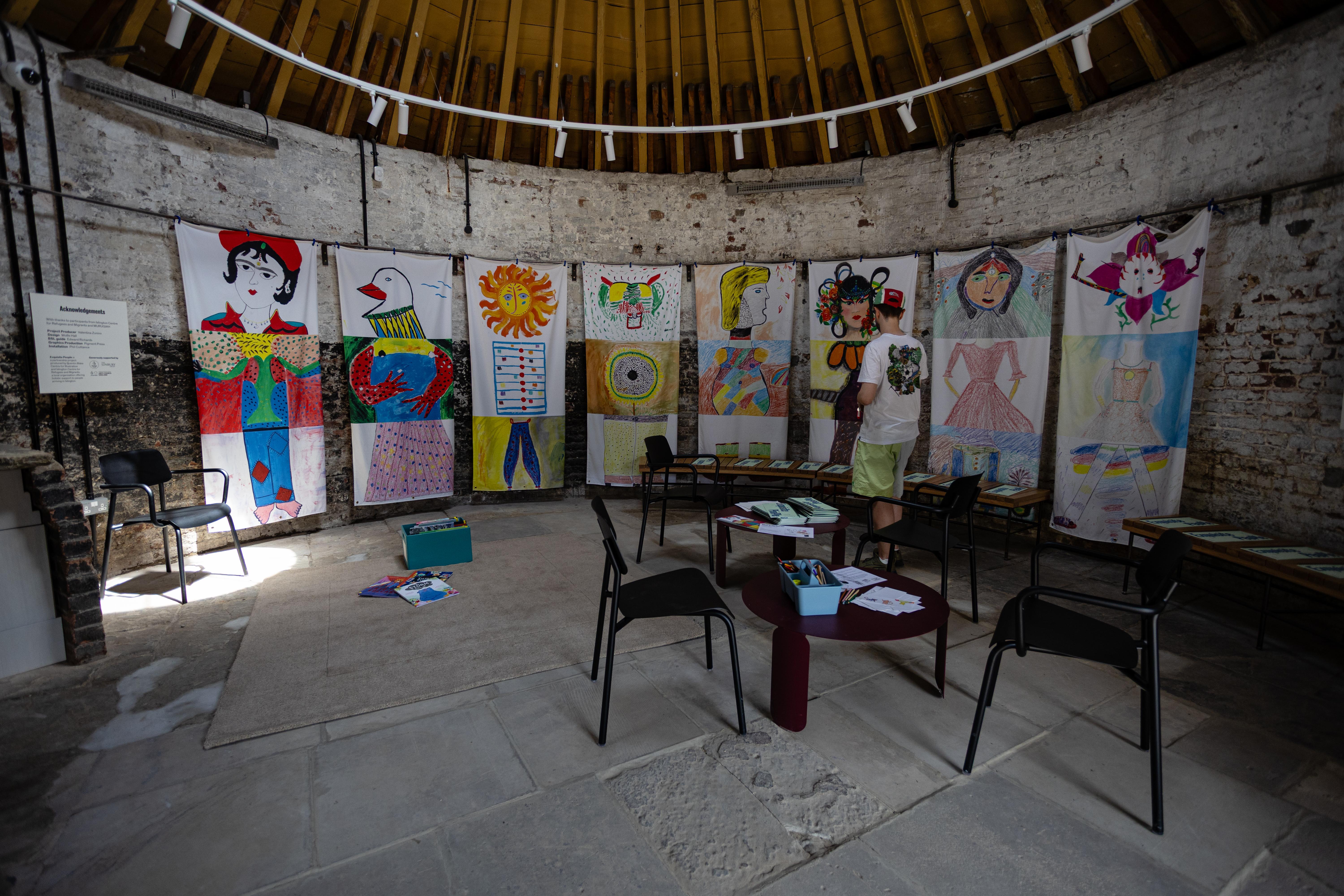 The interior of a round building with hanging fabrics each featuring an assembled head, body and neck drawn in different styles.