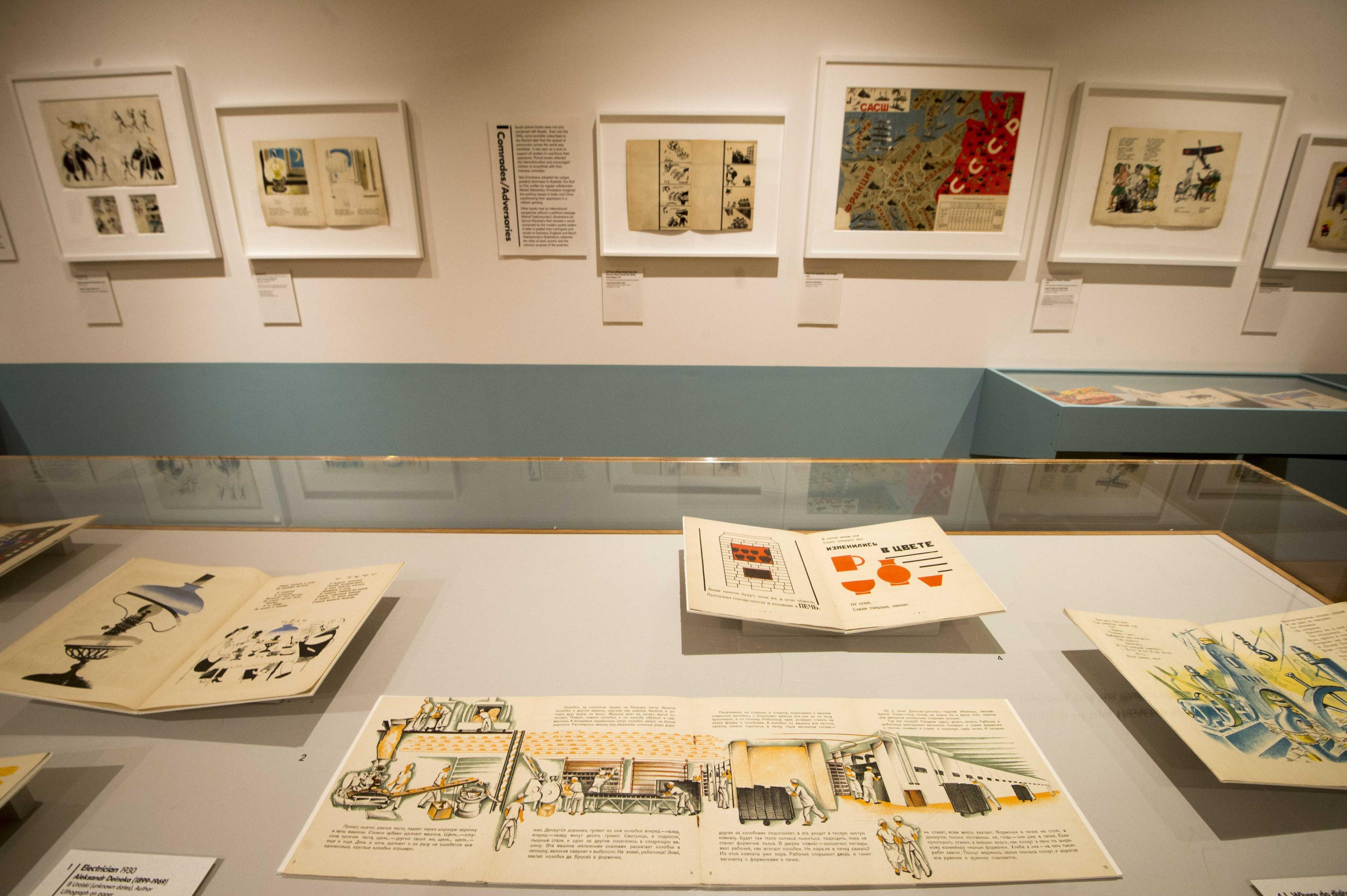 Inside an exhibition space with framed illustrations on the wall and displayed in a glass cabinet.