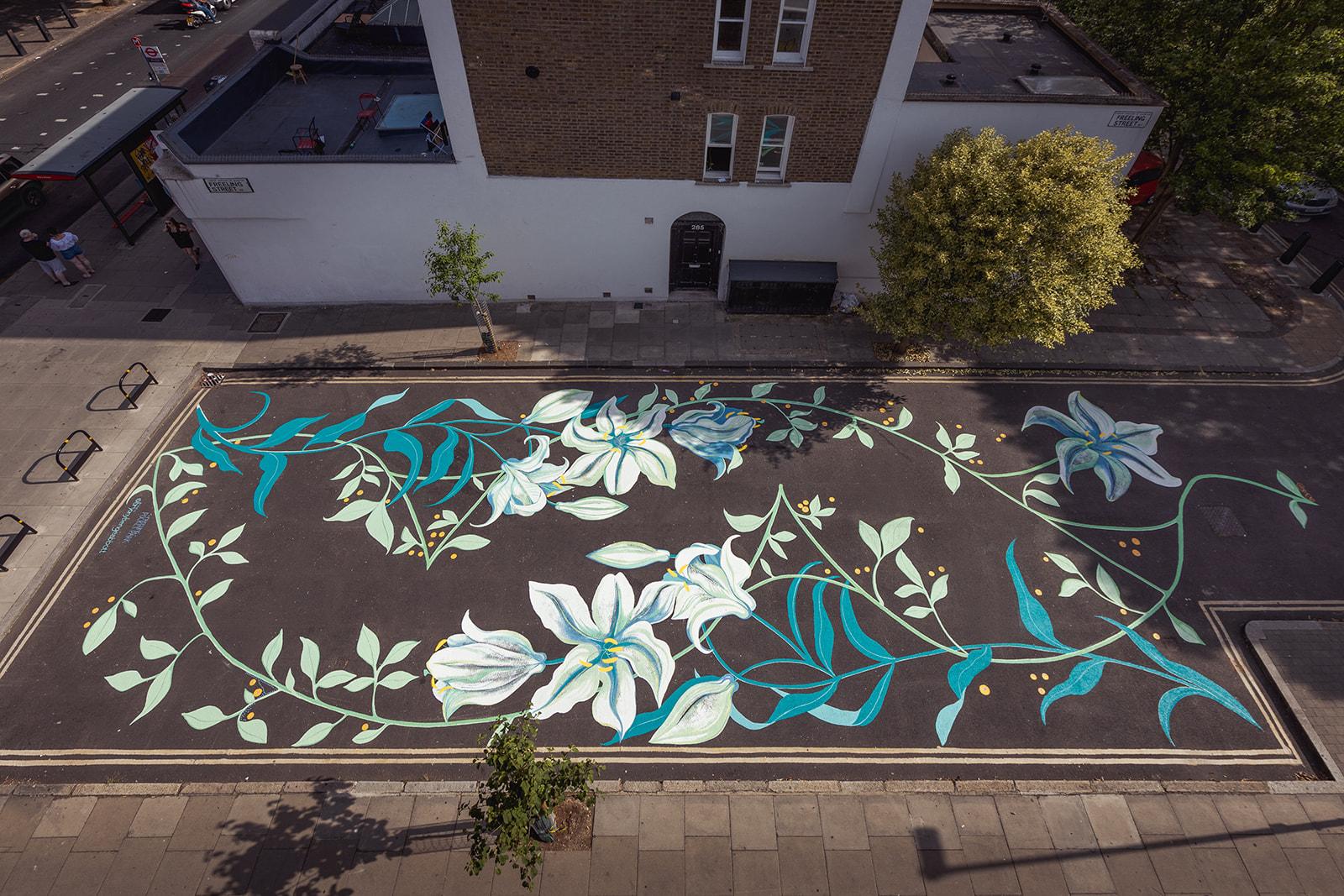 Photograph of a street with beautiful painted flowers. The flowers are white with blue leaves. 