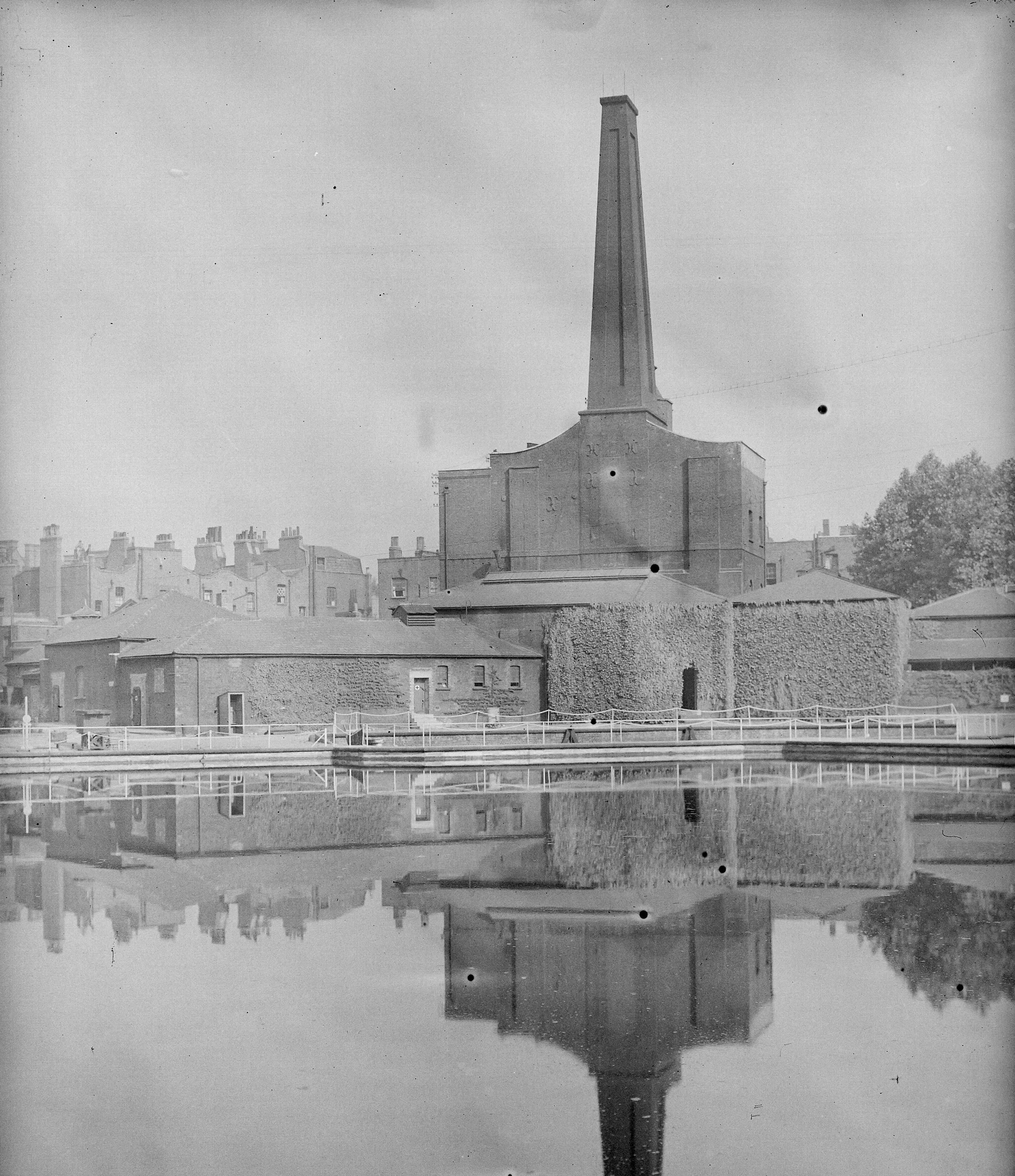 Photograph of industrial brick building with a tall chimney next to a reservoir