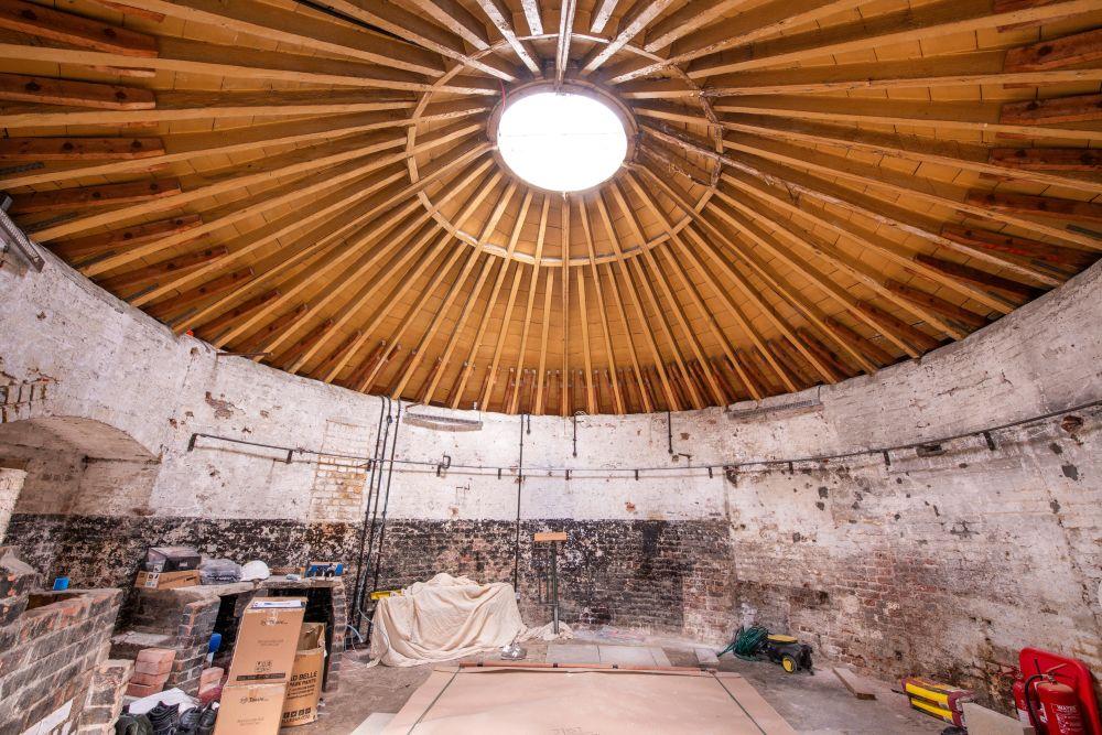 Interior of a circular room with exposed wooden beams and a skylight, tools are scattered on the floor