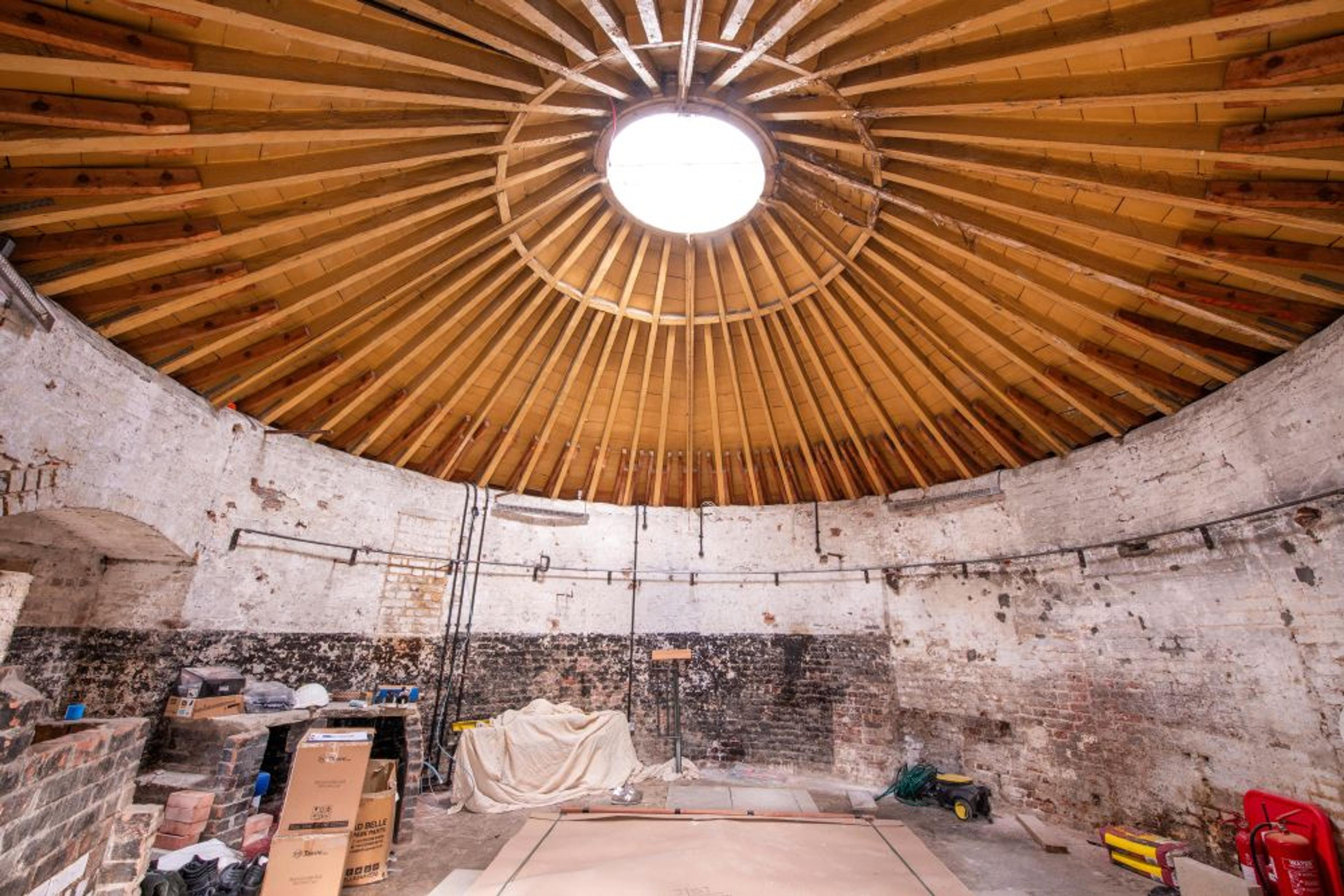Interior of a circular room with exposed wooden beams and a skylight, tools are scattered on the floor