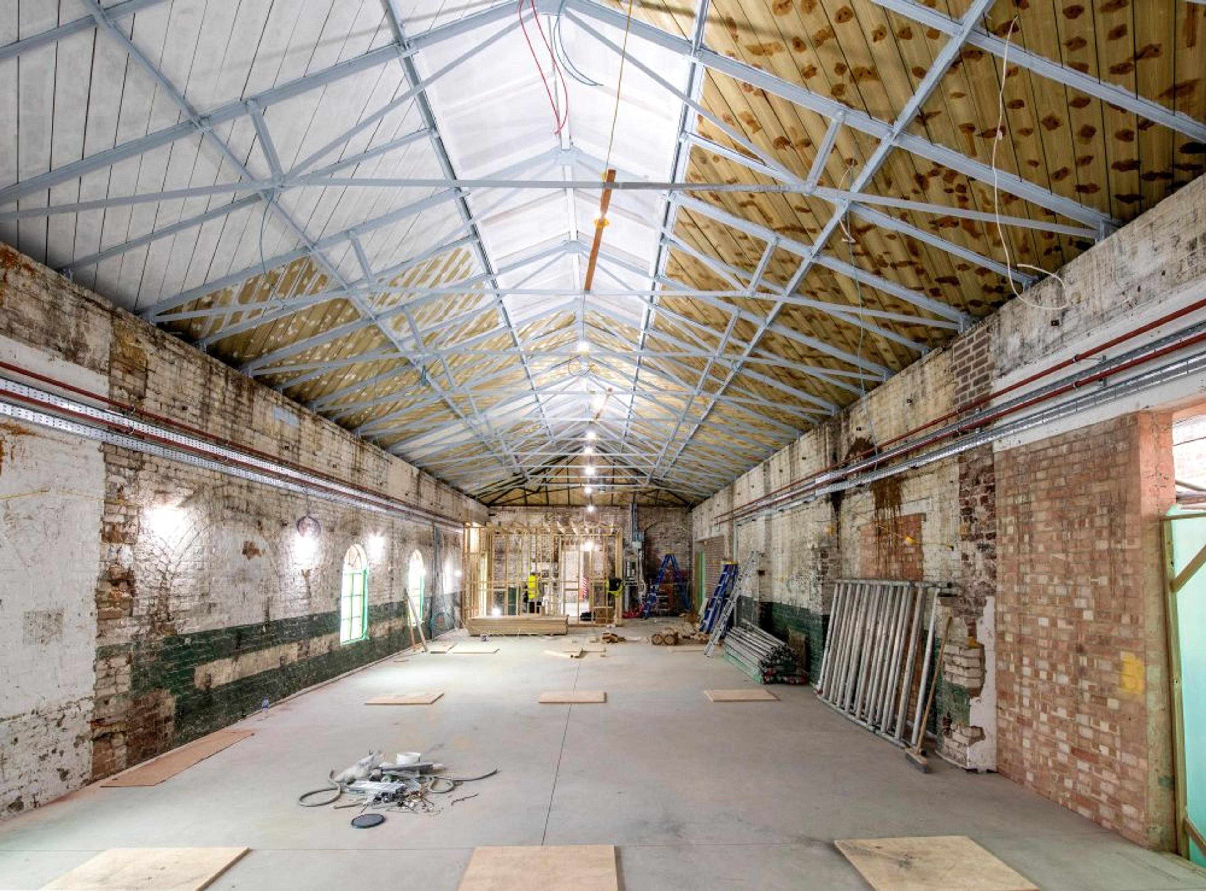Industrial space under renovation. There are exposed brick walls, a high vaulted ceiling with steel beams and materials. 