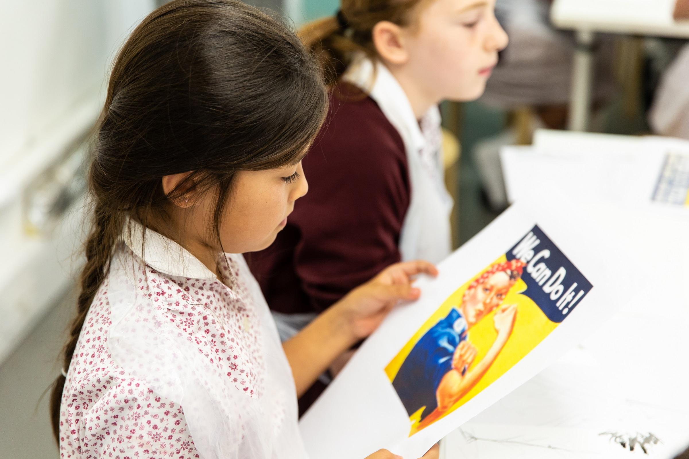 School pupil looking at a printout of a woman showing her bicep and the words 'we can do it'