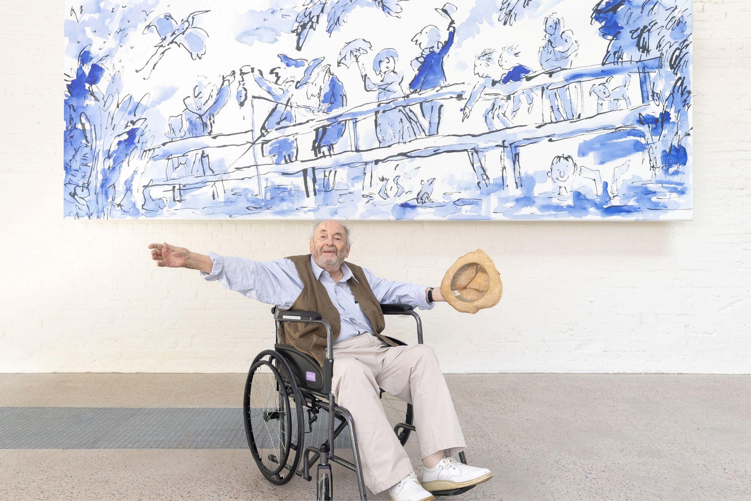 A man in a wheelchairs throws up his arms in front of a large mural 