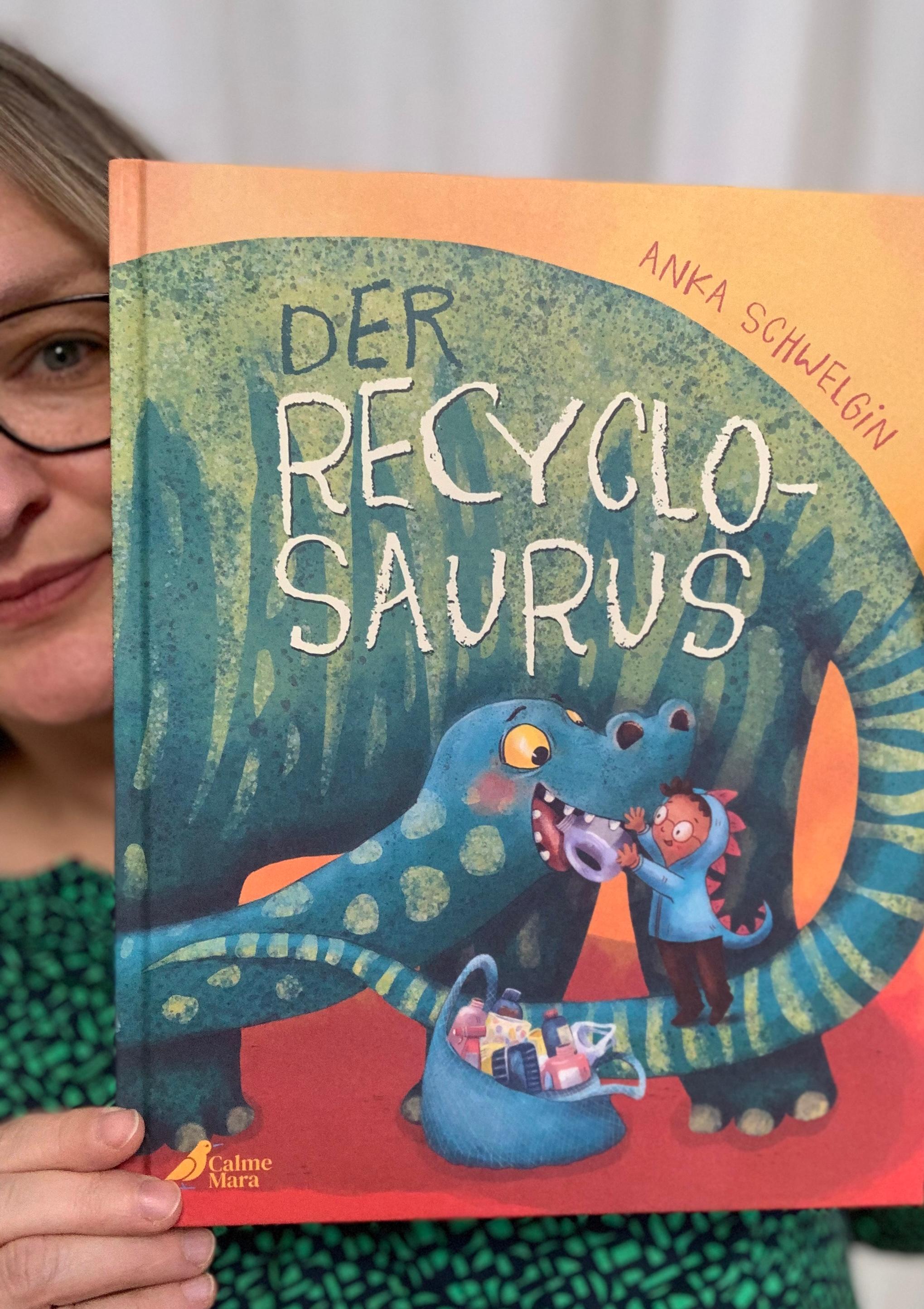 Person holds up a copy of a book 'Der Recyclosaurus'.