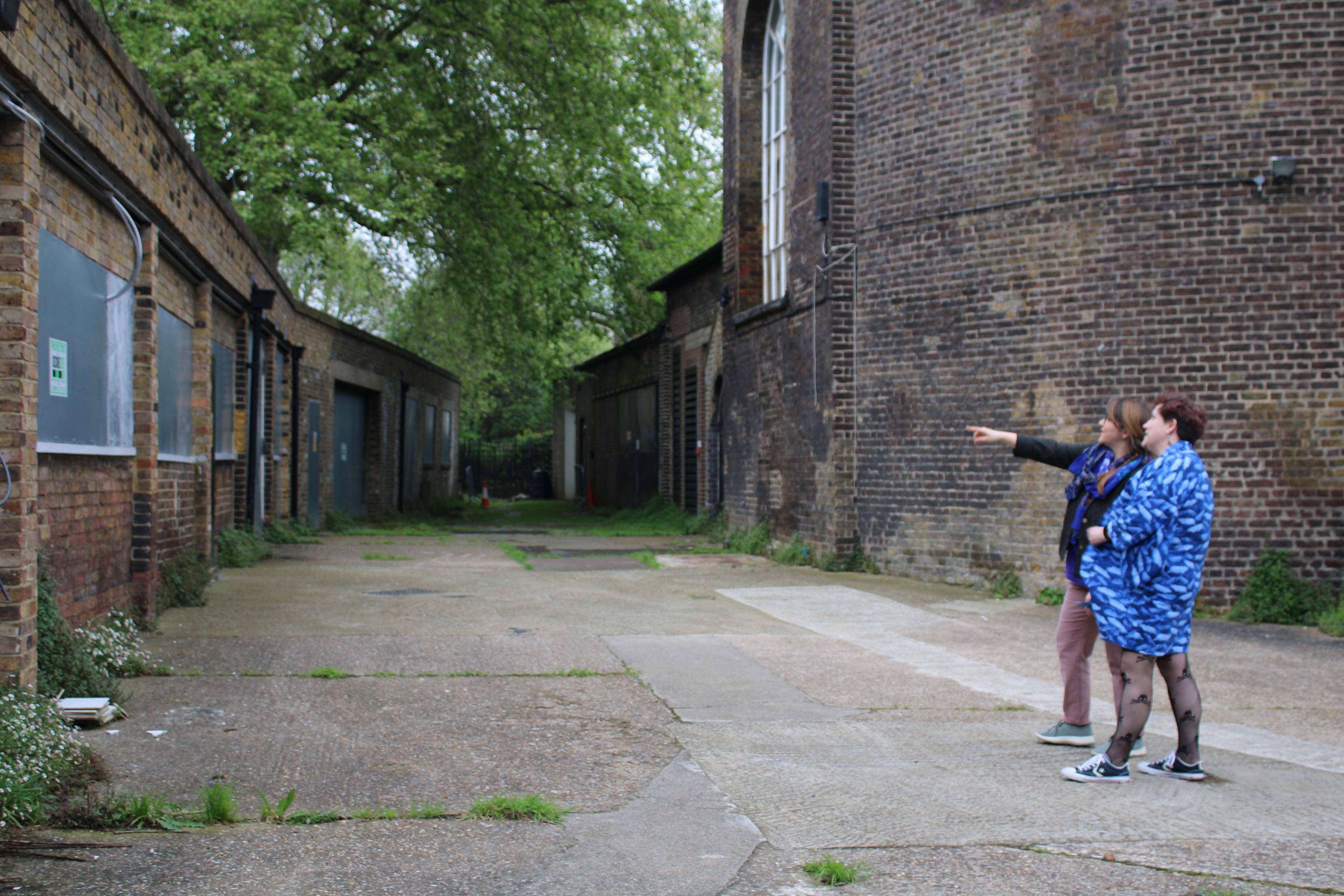 Two people standing in-between two brick buildings pointing at part of the building.