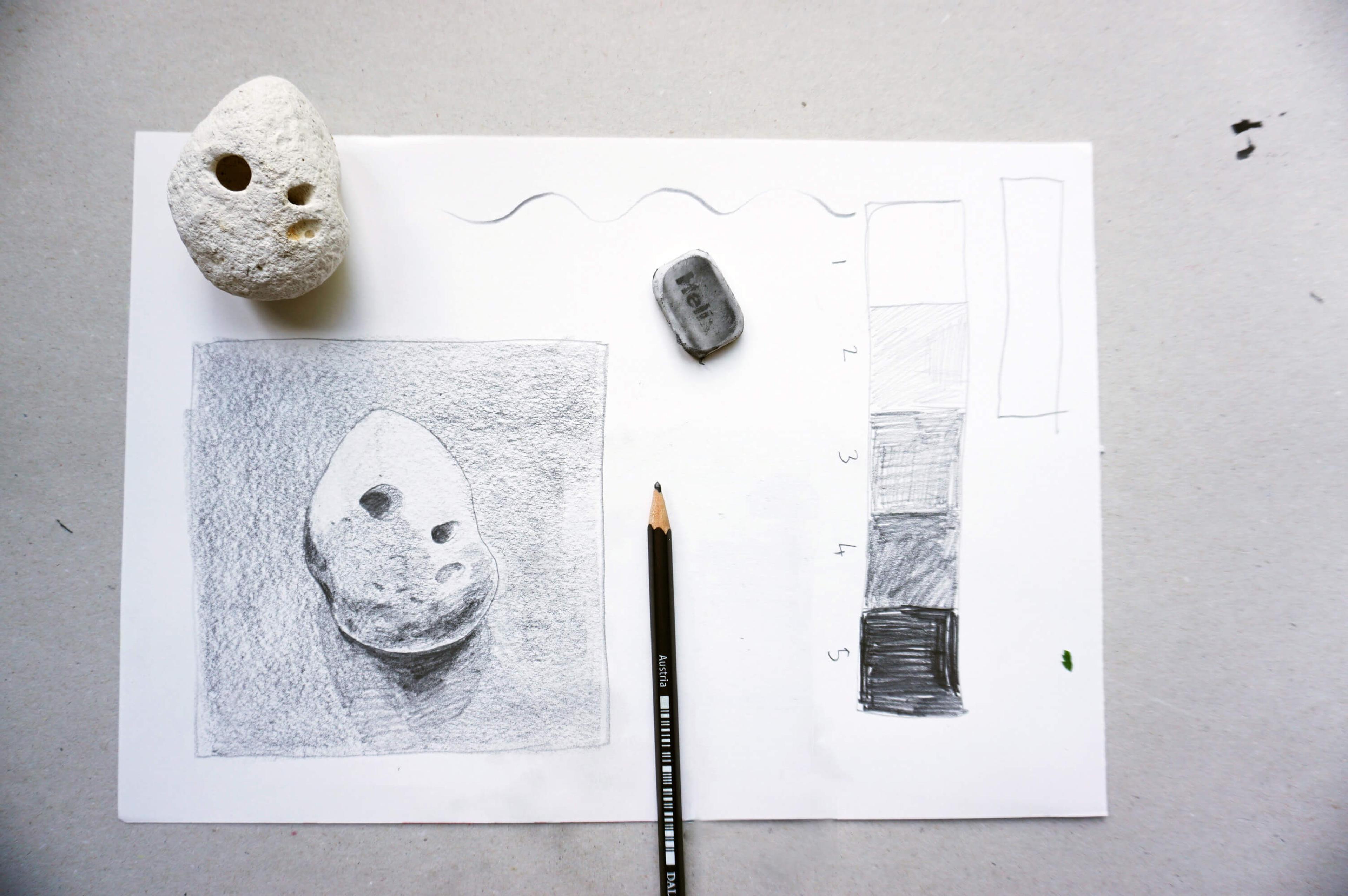 Photograph of a sheet of paper with the sketch of a rock. The rock in the drawing is placed on the sheet, along with a pencil and an eraser.