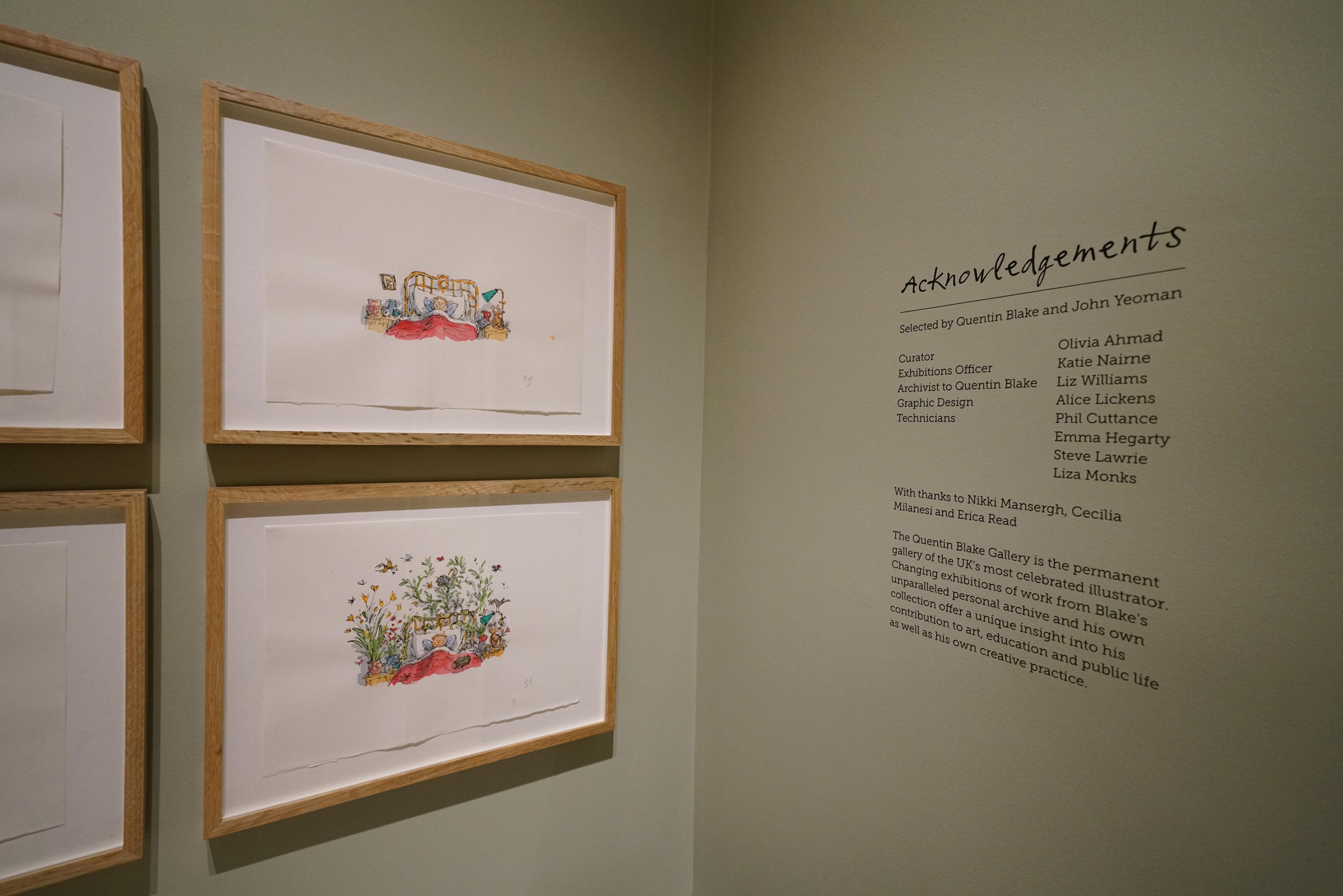 Framed illustrations and text displayed on a green wall in an exhibition space.